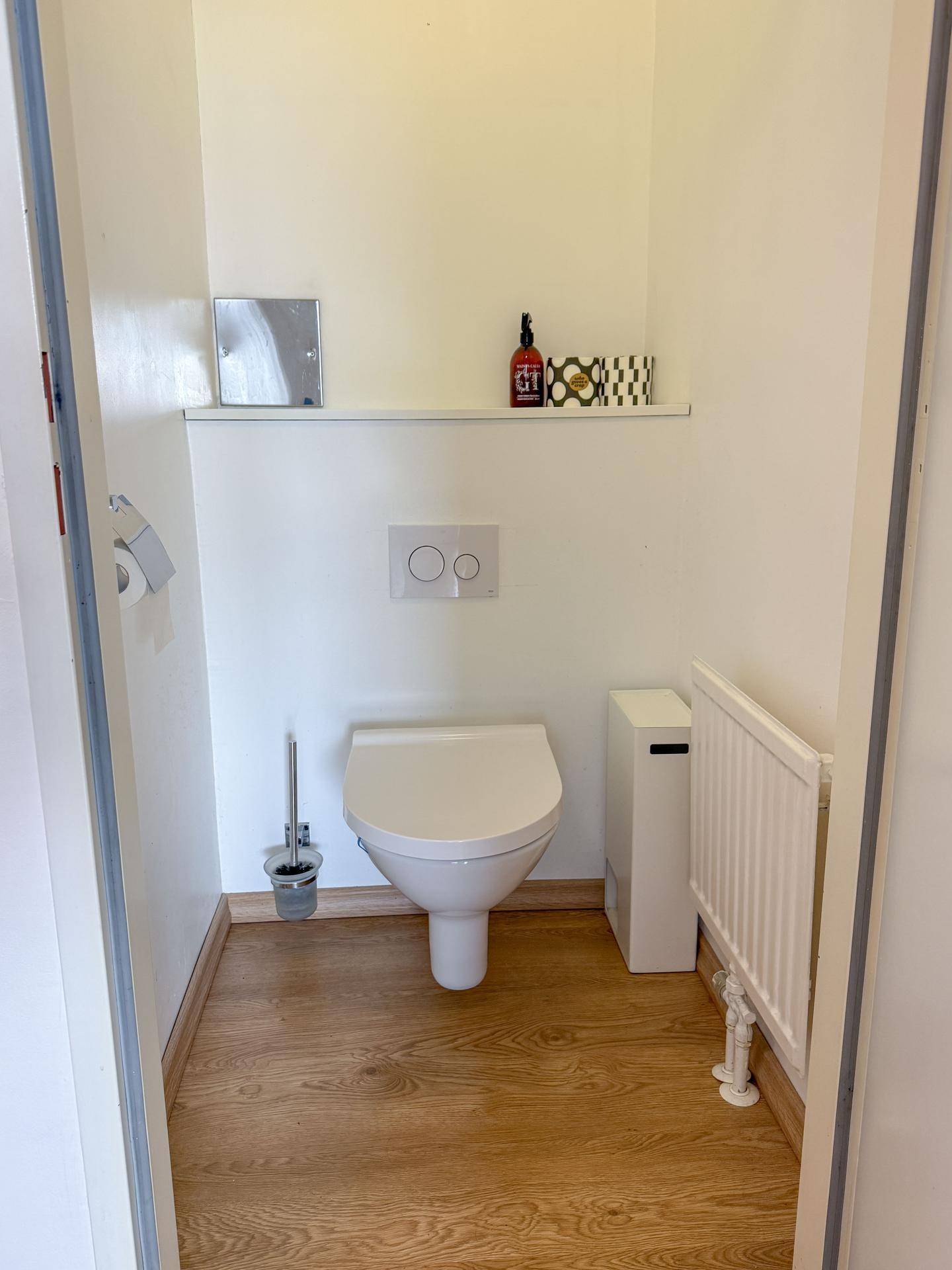 Kleines Gäste-WC mit wandhängender Toilette, Heizkörper und Holzboden.