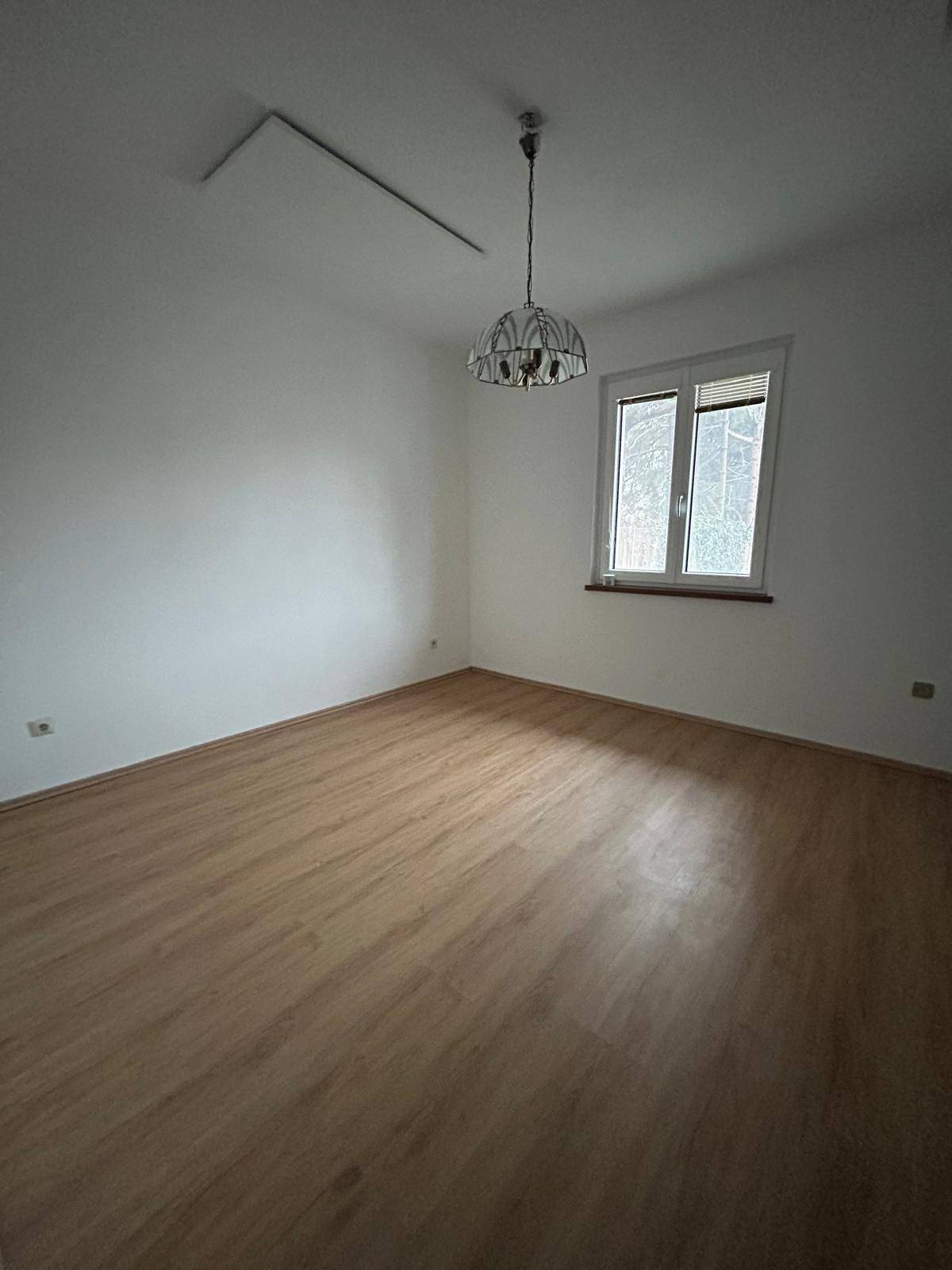 Helles Schlafzimmer mit Laminatboden, weißen Wänden und einer einfachen Deckenleuchte.