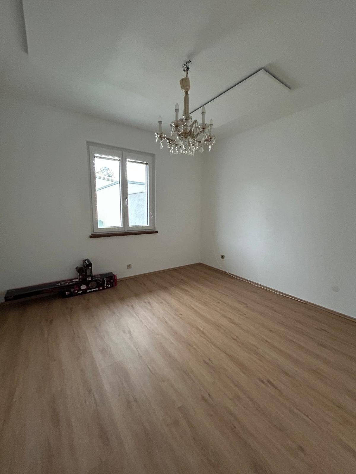 Helles Zimmer mit Laminatboden, weißen Wänden und einem klassischen Kronleuchter.