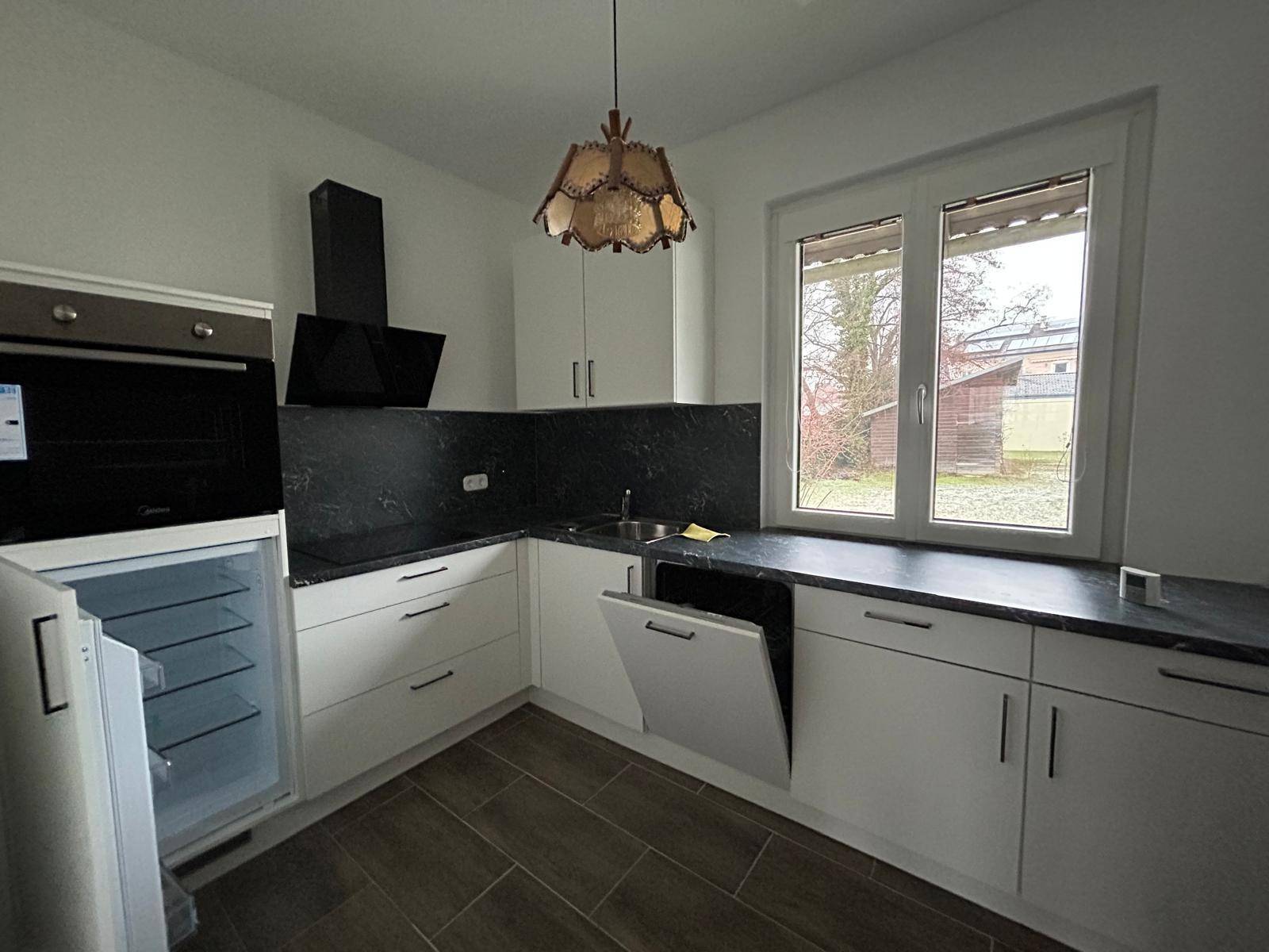 Moderne Küche mit weißen Schränken, dunkler Arbeitsplatte und integrierten Geräten.