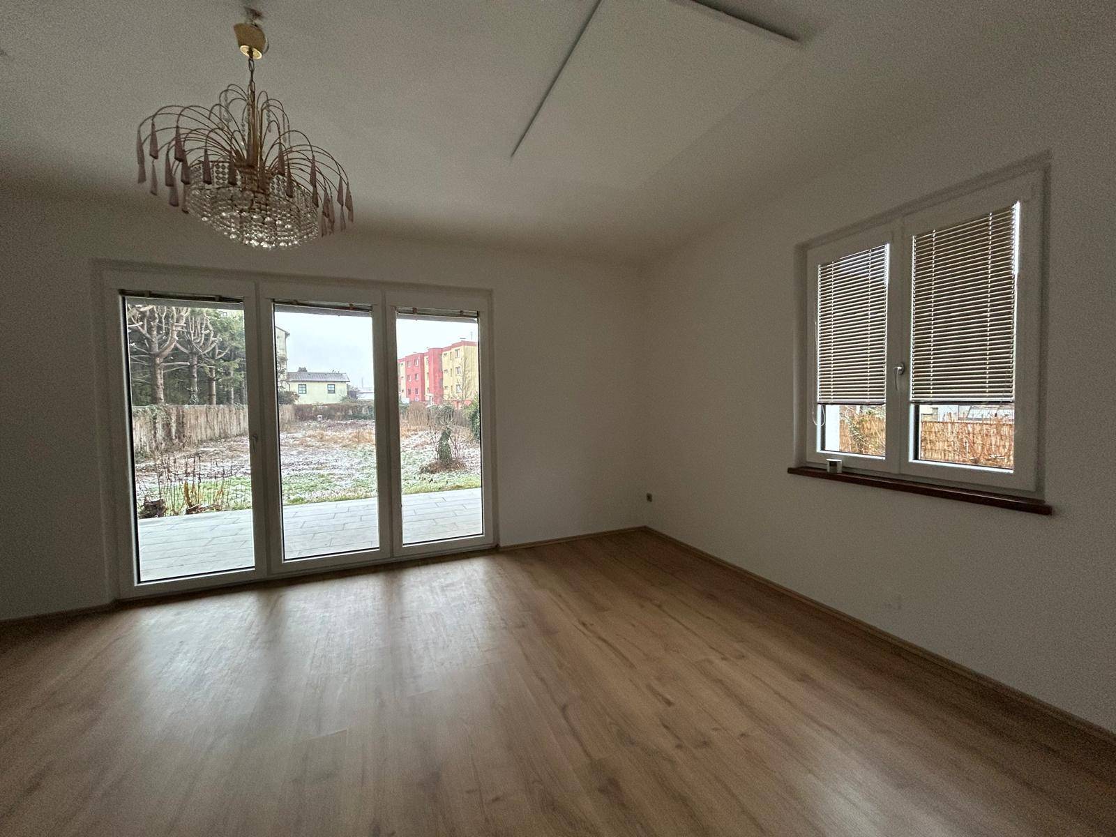 Geräumiges Zimmer mit Laminatboden, großen Fenstern und direktem Zugang zum Außenbereich.