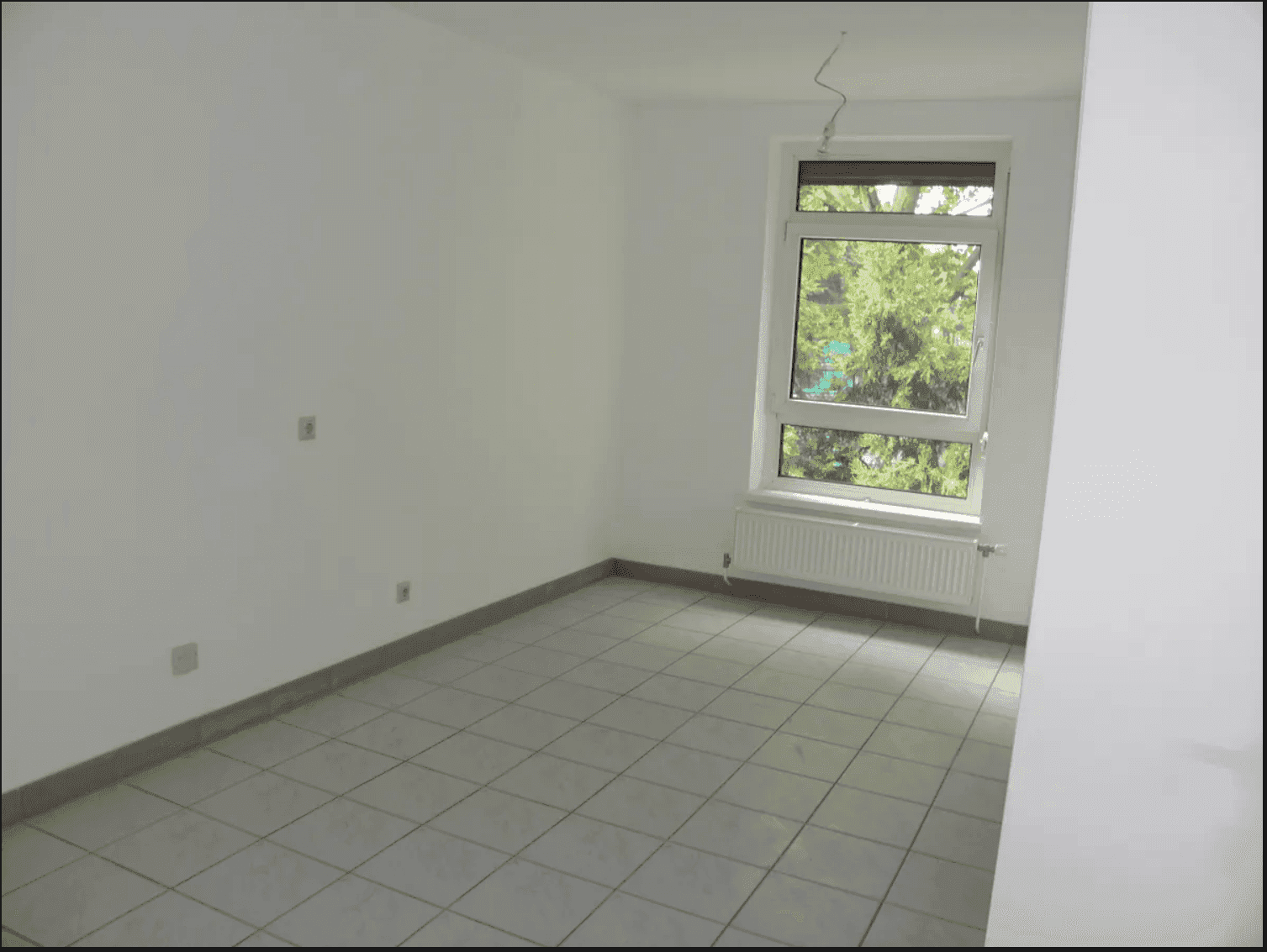 Leerer Raum mit hellen Fliesen und einem Fenster, das eine angenehme natürliche Beleuchtung bietet.