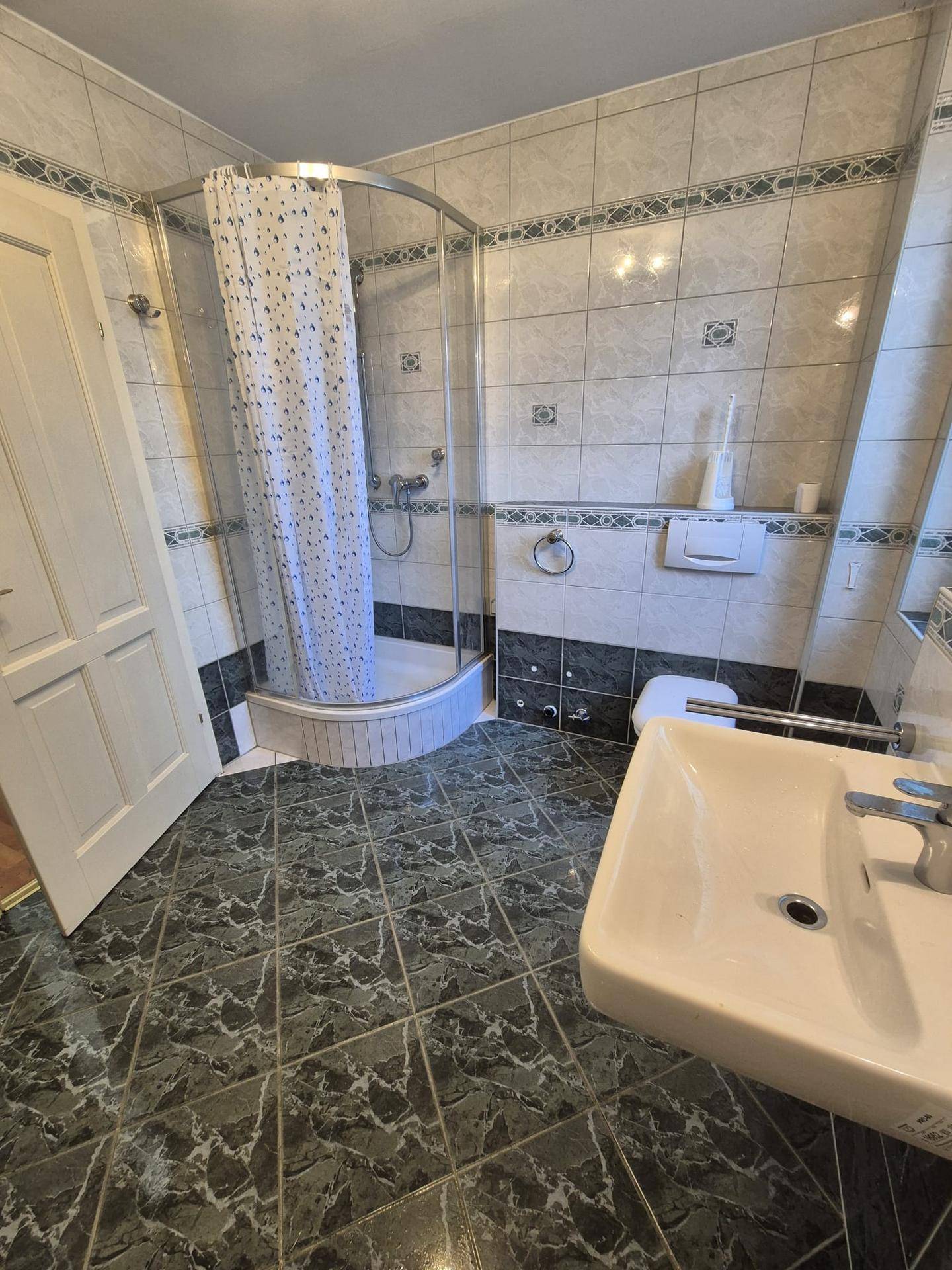 Badezimmer mit Duschkabine, WC und Waschbecken, komplett gefliest in dunklen und hellen Tönen.
