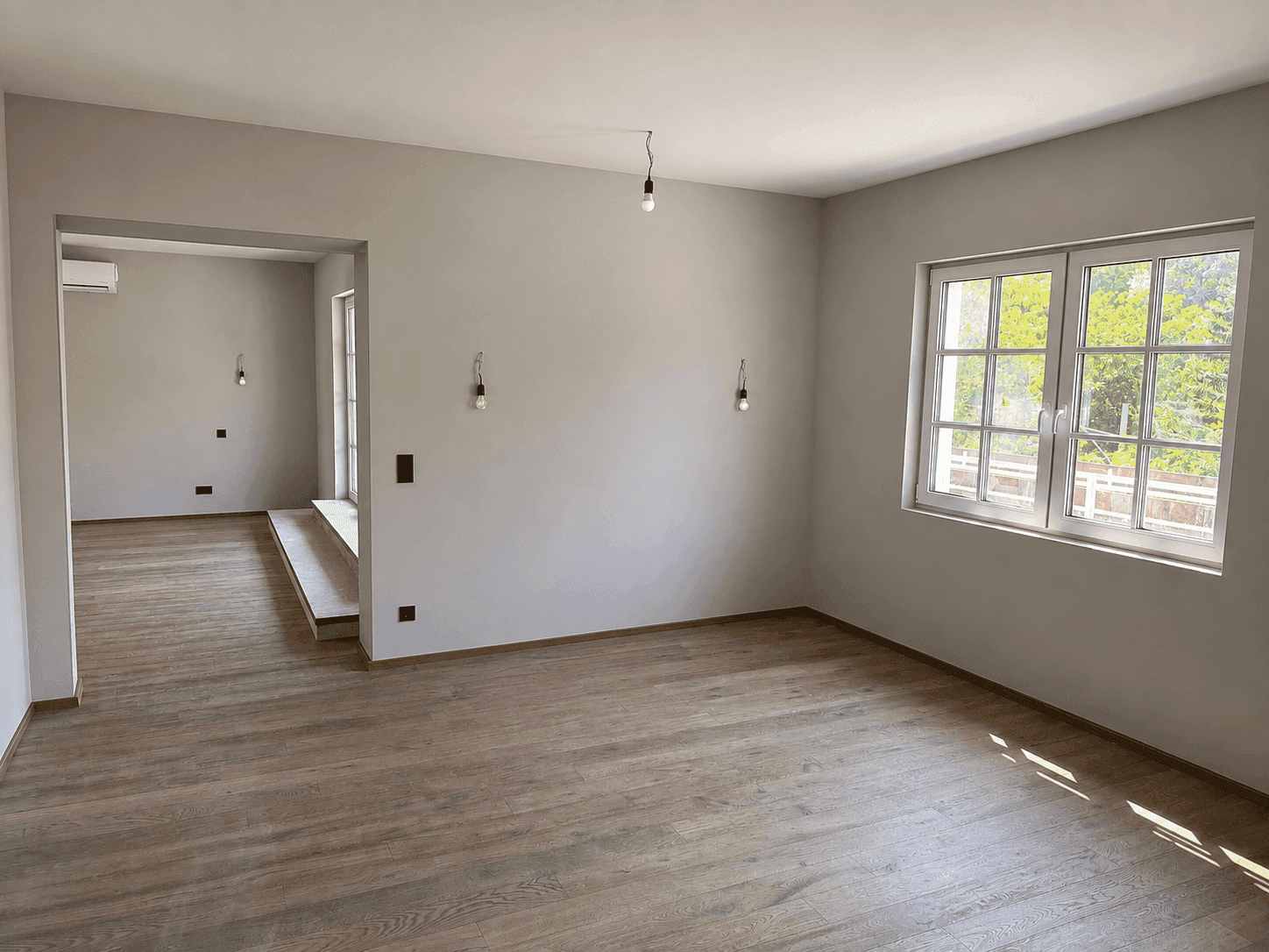 Helles Wohnzimmer mit Holzboden, großen Fenstern und einer Klimaanlage.