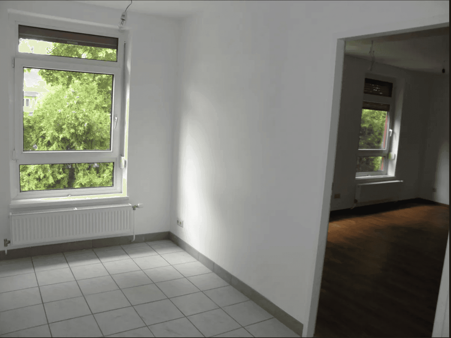 Heller Raum mit Fliesenboden und einem Fenster, das einen Blick ins Grüne ermöglicht.