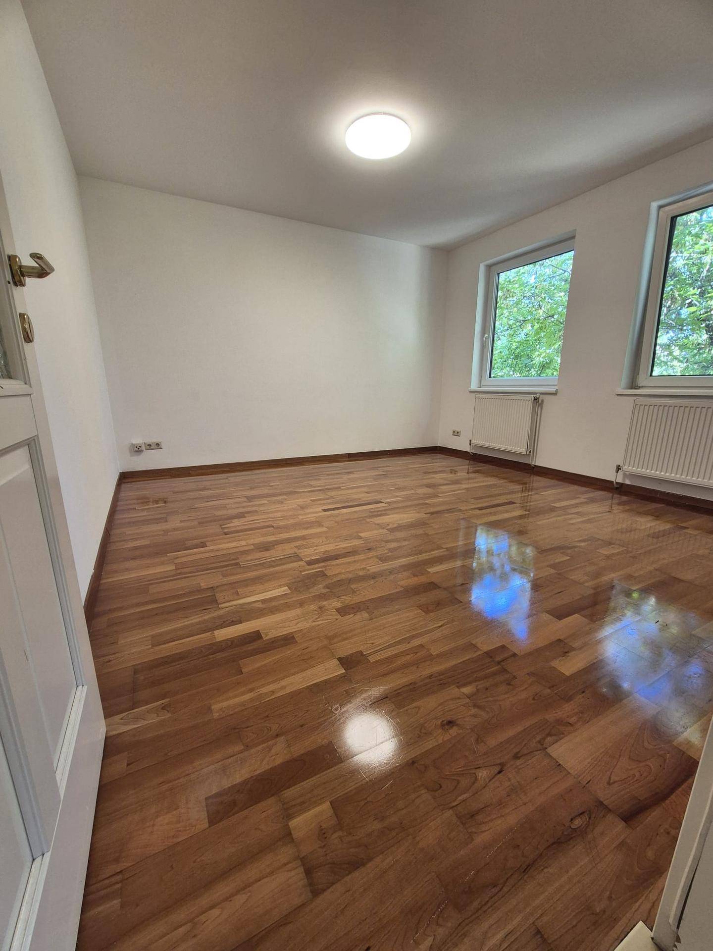 Geräumiges Zimmer mit Holzboden und viel Tageslicht, ideal als Schlaf- oder Arbeitszimmer.