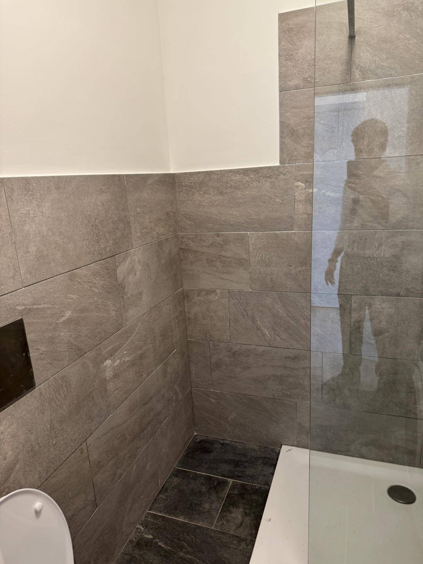 Ebenerdige Dusche mit Glasabtrennung und grauen Wand- und Bodenfliesen in modernem Design.