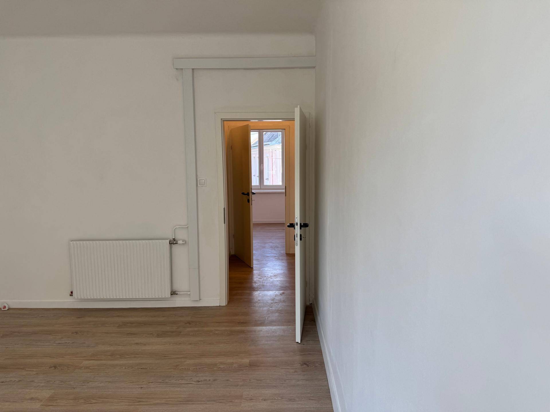 Heller Innenraum mit Laminatboden und Blick durch eine offene Tür in einen weiteren Raum.