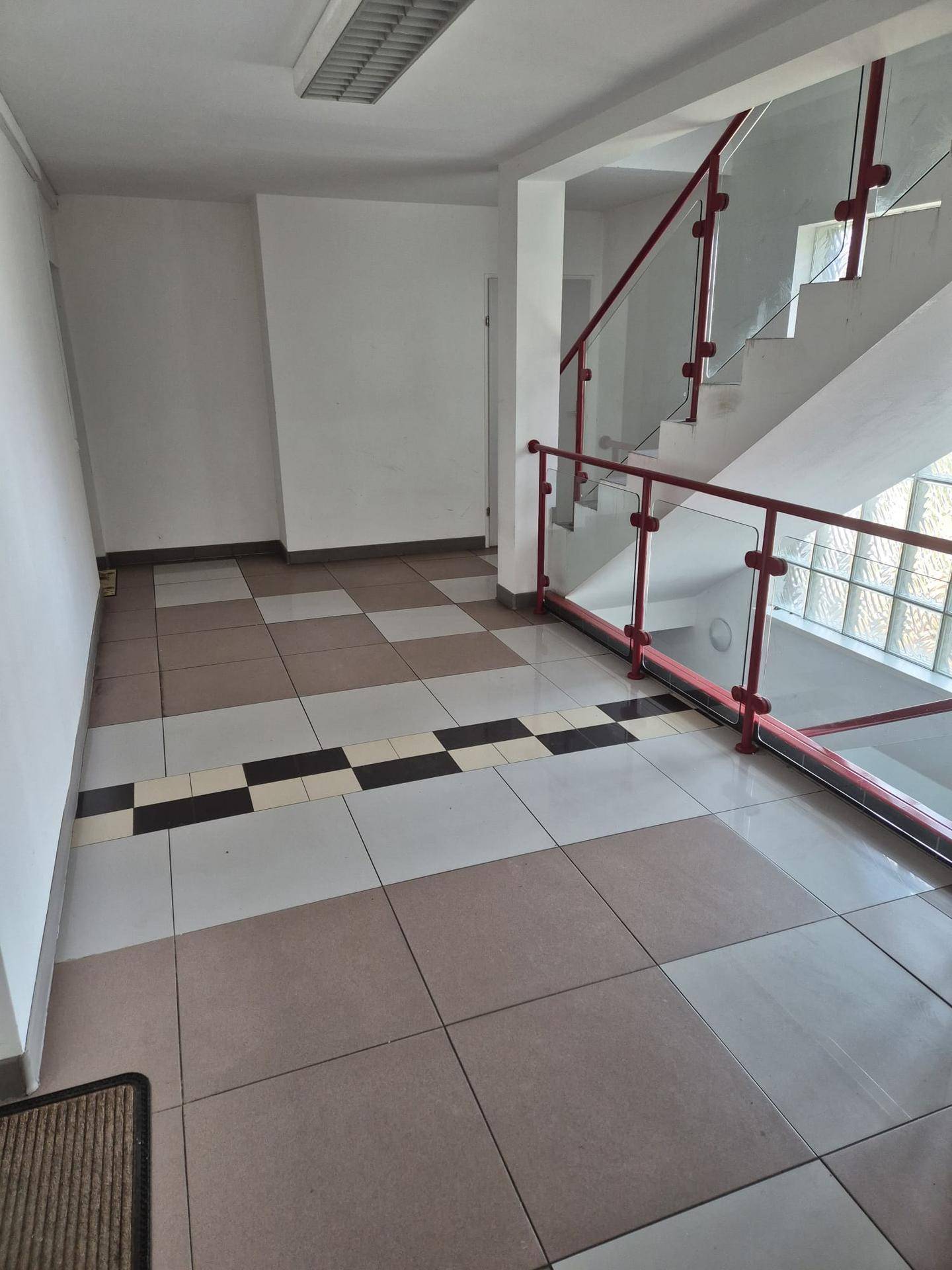 Heller Flur mit gemustertem Fliesenboden und Treppenaufgang mit rotem Glasgeländer.