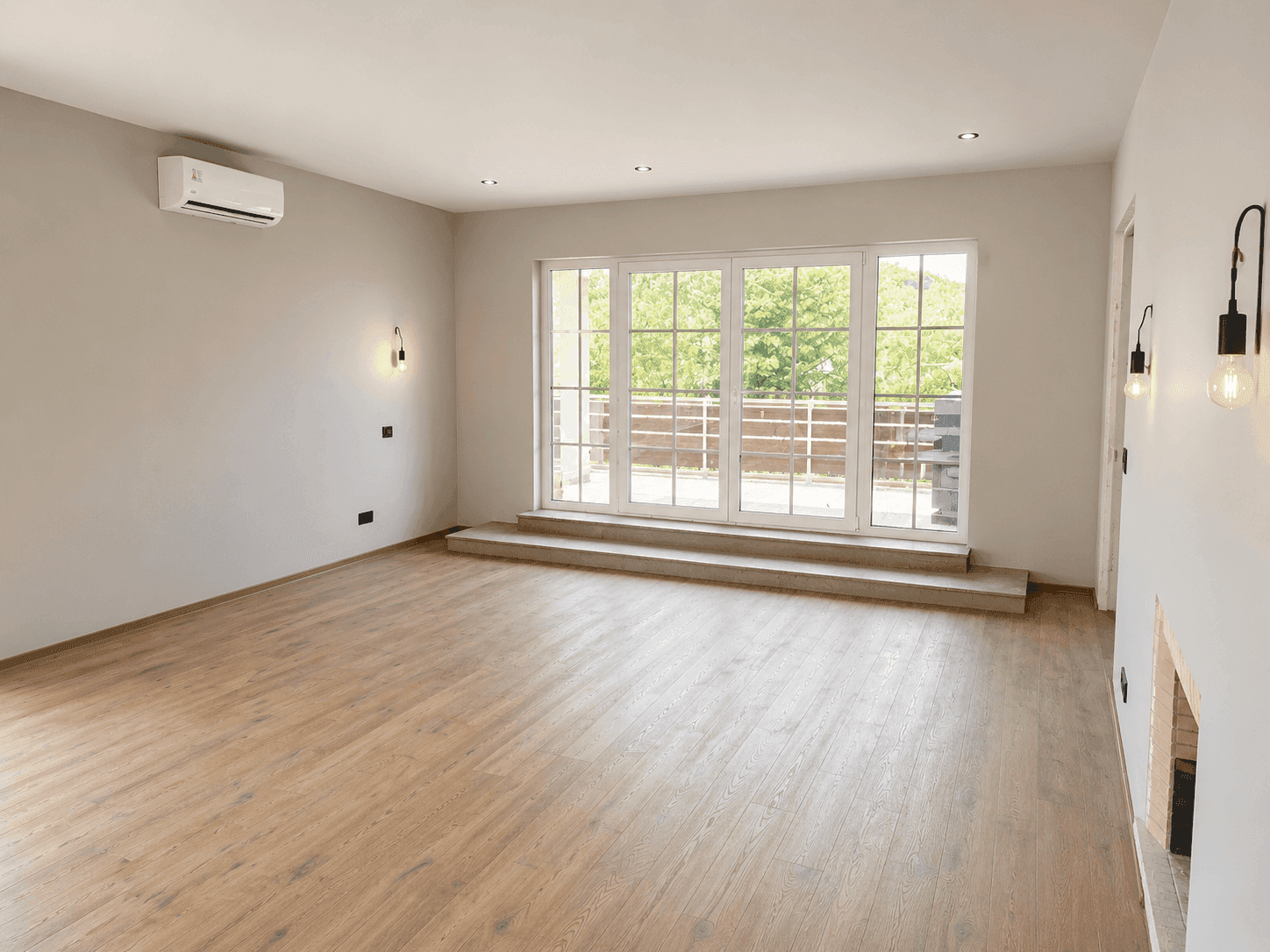 Geräumiges Wohnzimmer mit Holzboden, Klimaanlage, Kamin und Zugang zur Terrasse.
