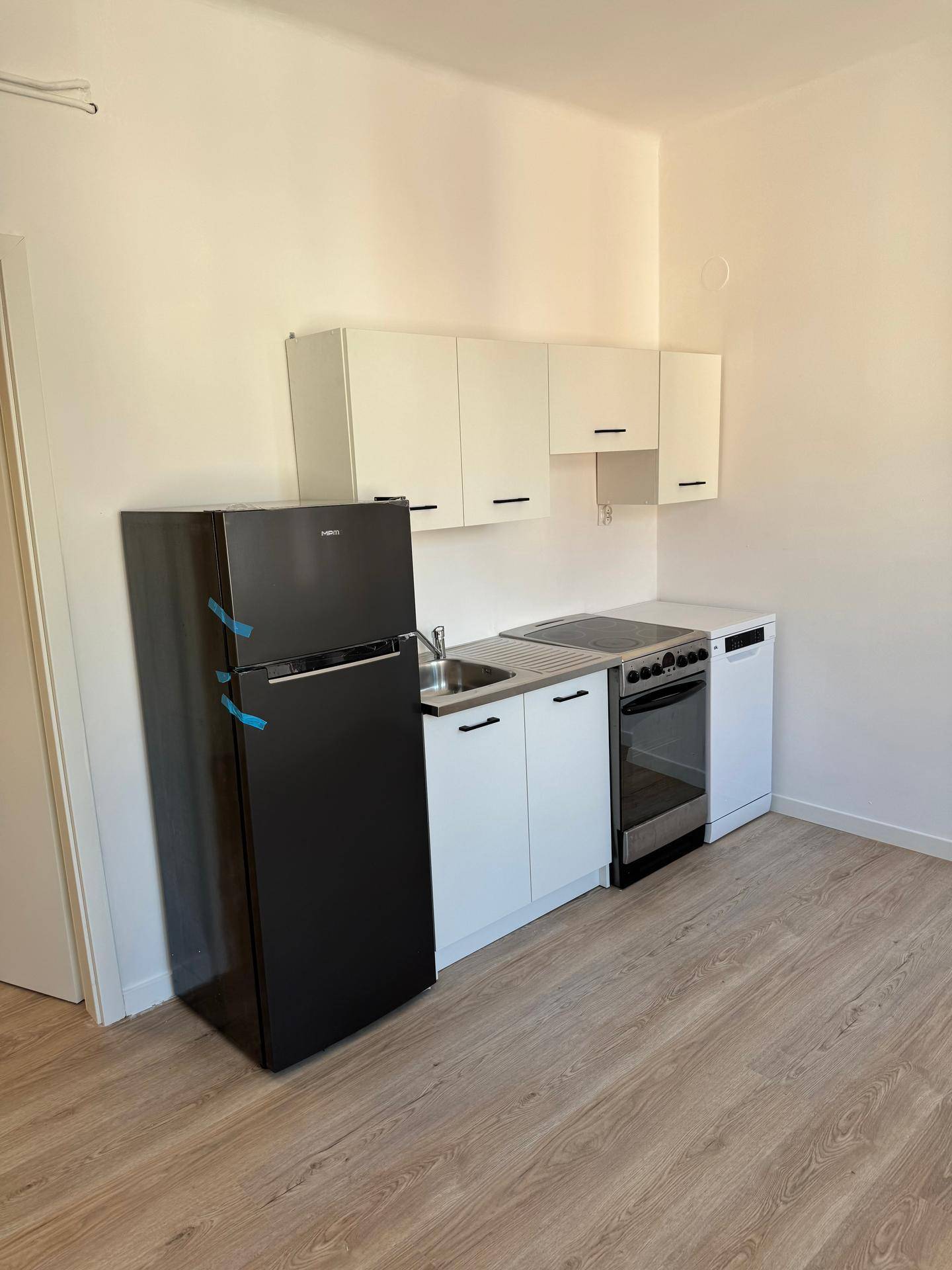 Neue Einbauküche mit weißen Schränken, schwarzem Kühlschrank und integriertem Kochfeld und Ofen.