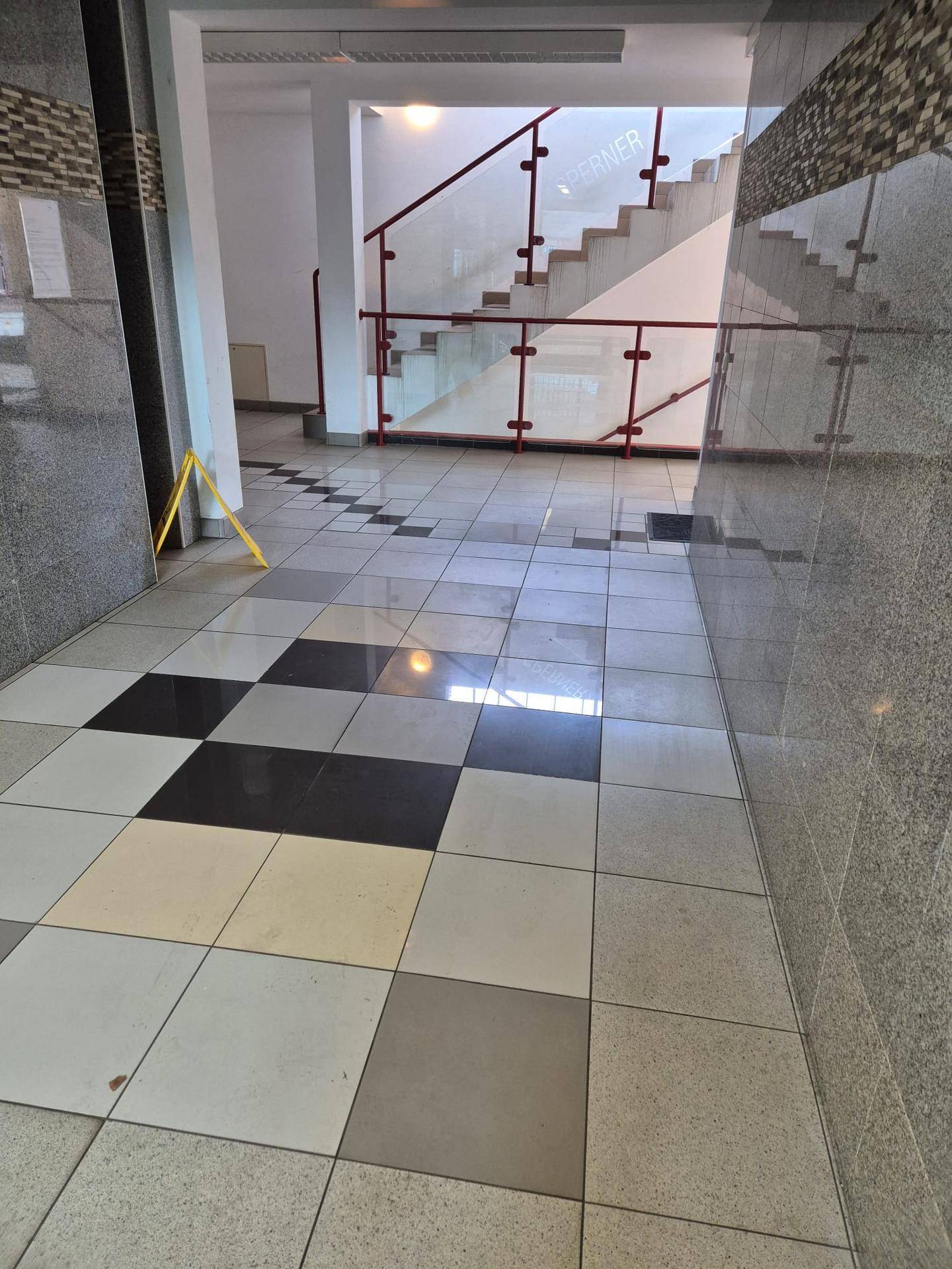 Eingangsbereich mit gemustertem Fliesenboden und einer modernen Treppe mit rotem Geländer.