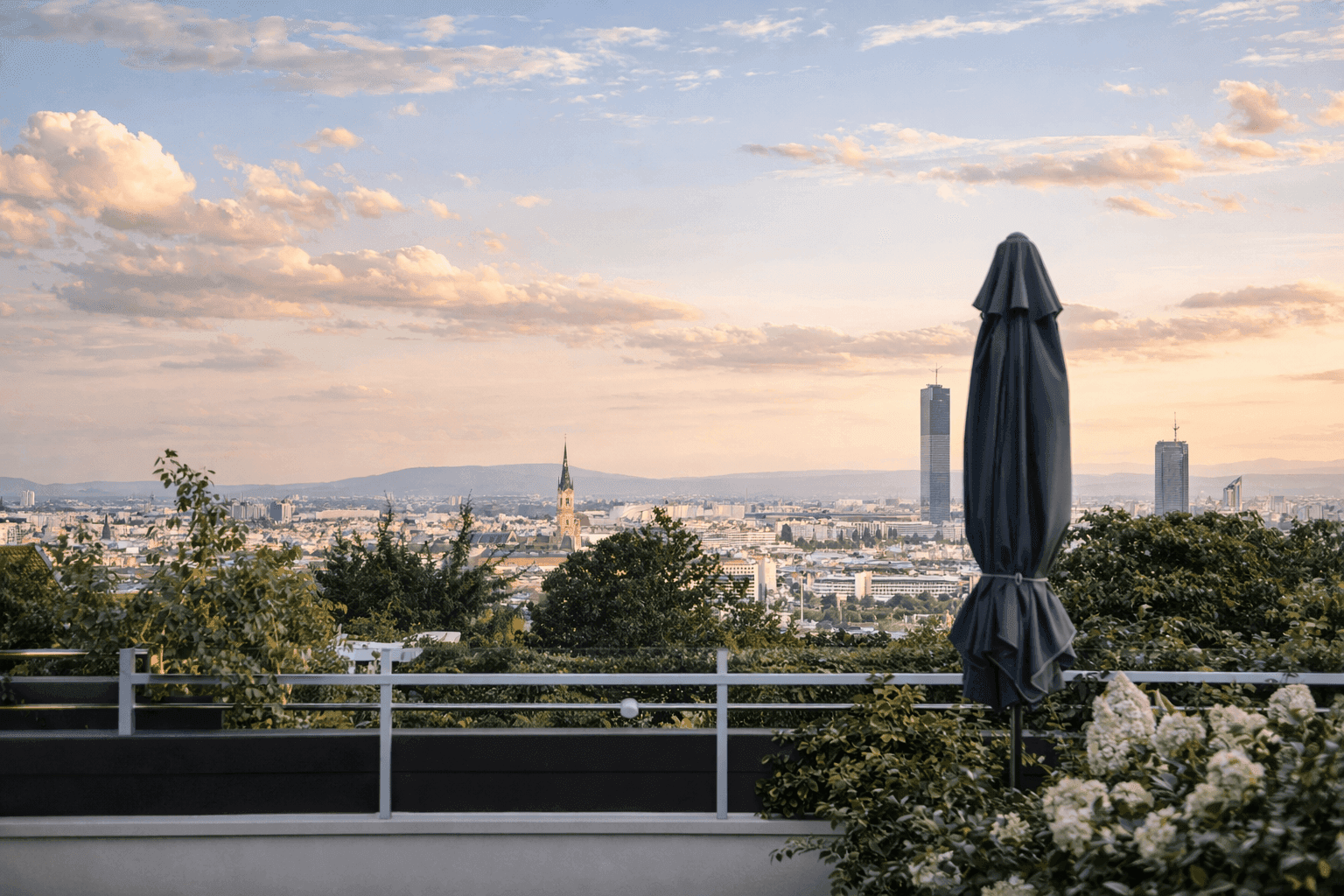 Panoramablick über die Stadt von einer großzügigen Terrasse mit Sonnenschirm bei Sonnenuntergang.