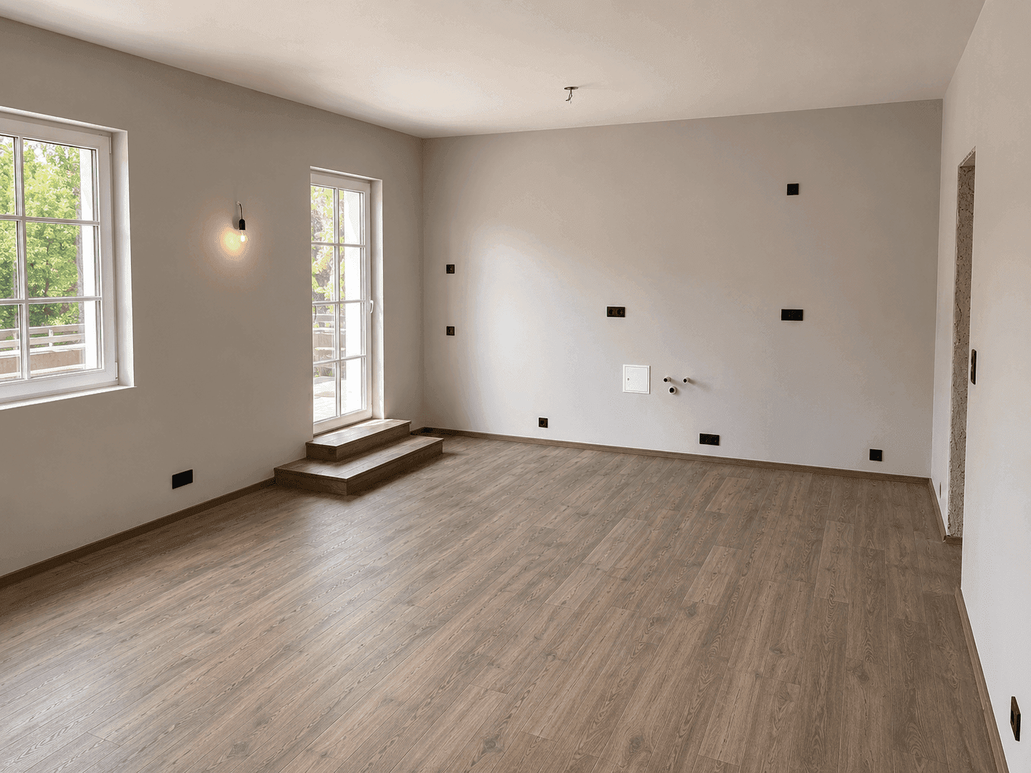 Leerer Raum mit Holzboden und Zugang nach draußen, vorbereitet für eine Küche.