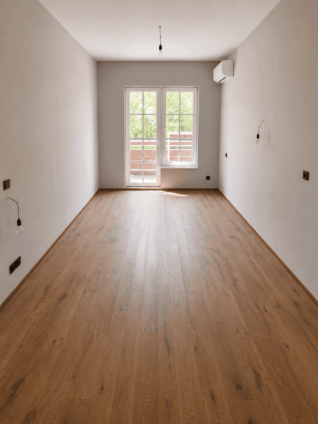 Heller Raum mit Holzboden, Klimaanlage und Zugang zu einem Balkon oder einer Terrasse.