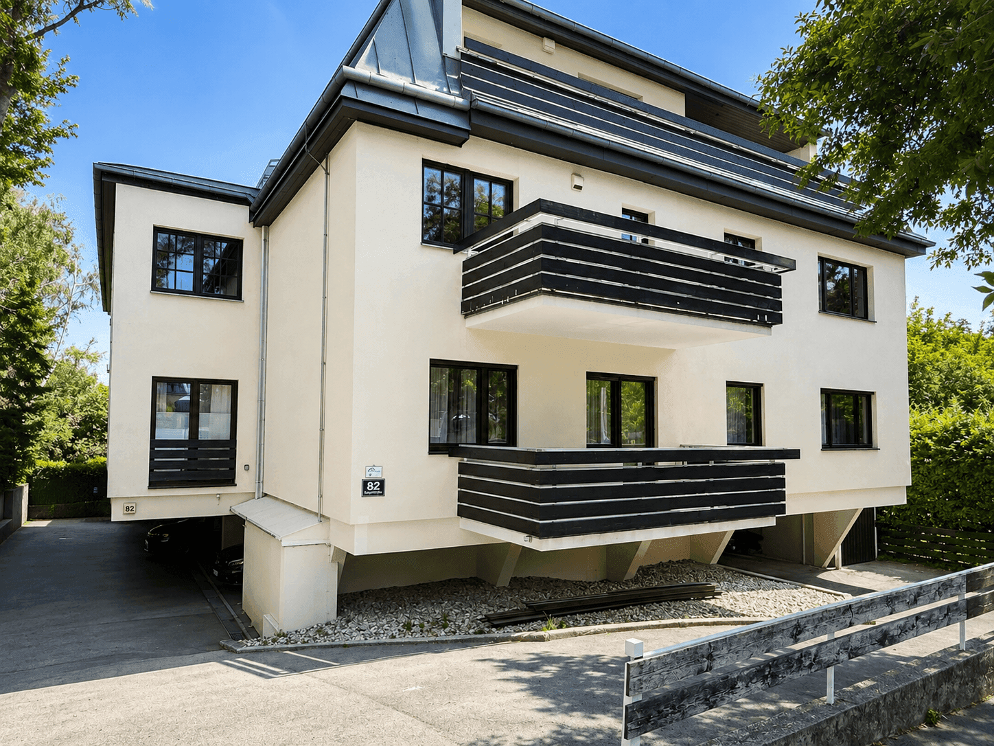 Modernes Mehrfamilienhaus mit weißer Fassade und schwarzen Balkonen unter blauem Himmel.