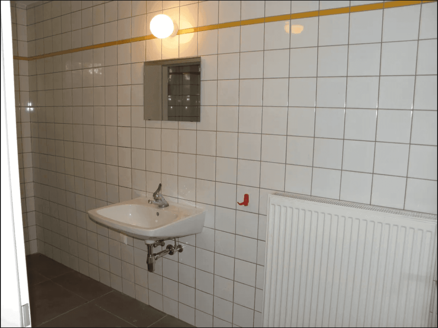 Badezimmer mit Waschbecken, Heizkörper und weißen Fliesen, die durch eine gelbe Linie akzentuiert sind.