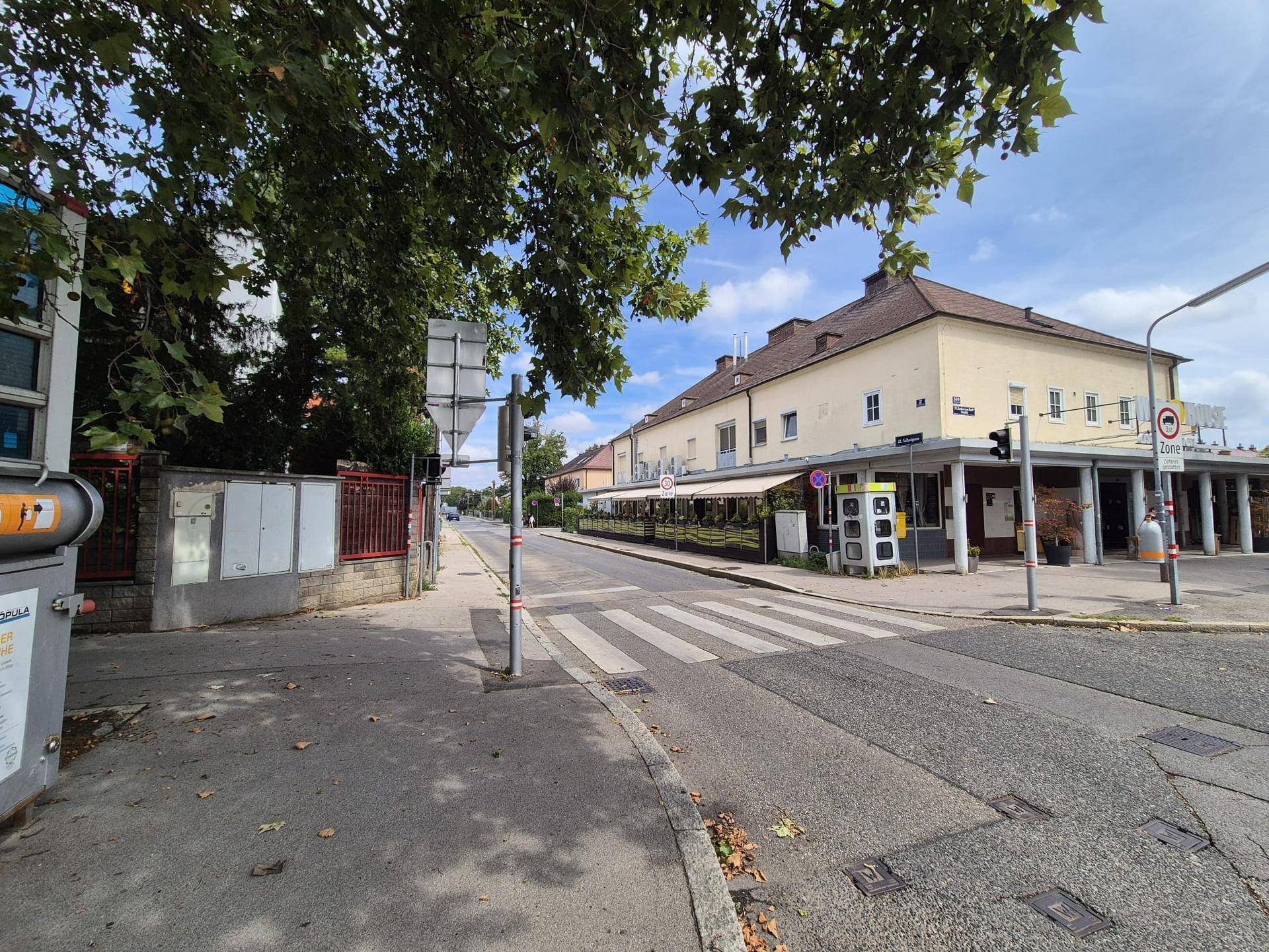 Straßenansicht mit einem Gebäude, Bäumen und einem Zebrastreifen, typisch für die Umgebung.