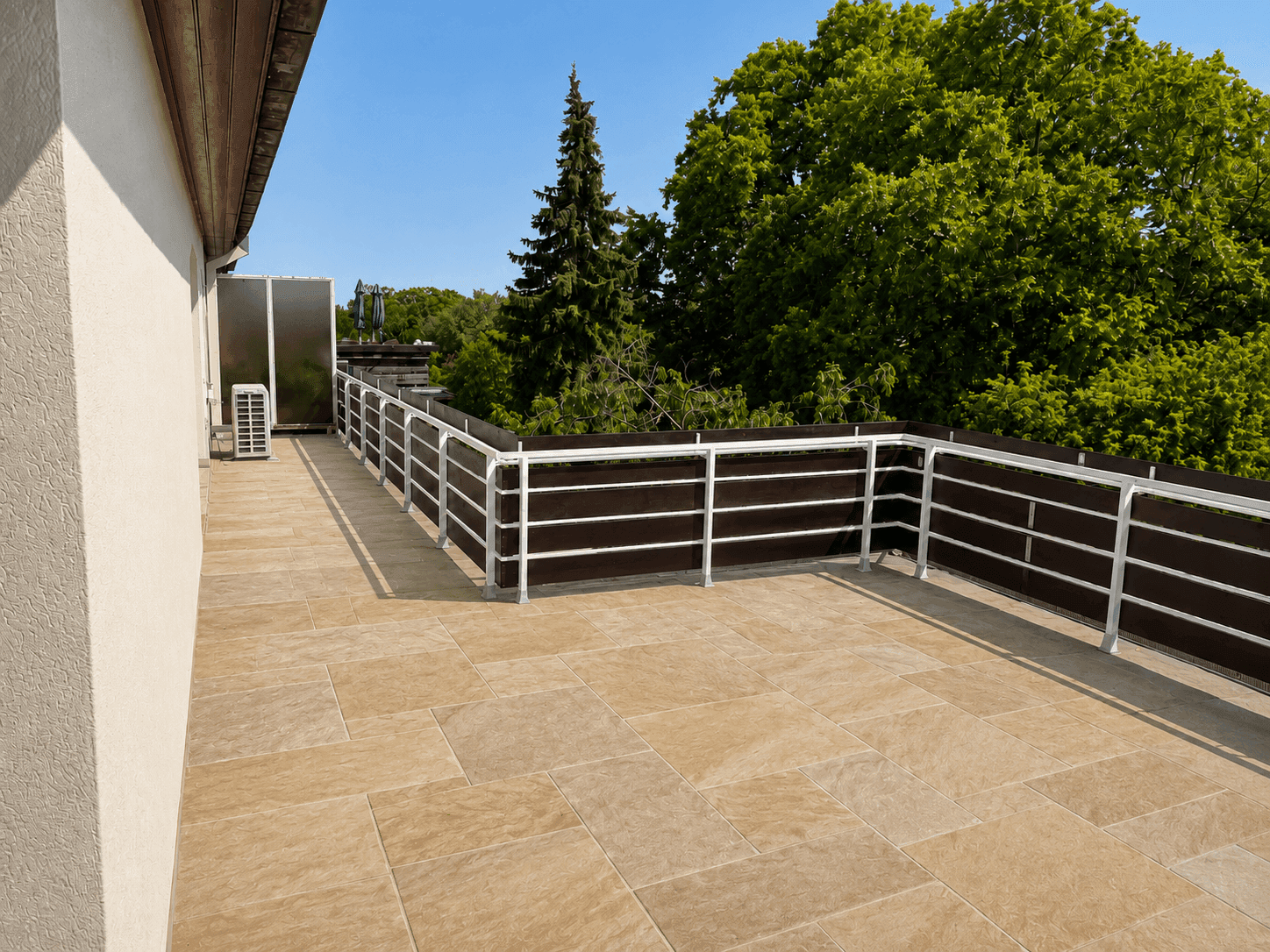 Große, geflieste Terrasse mit modernem Geländer und Blick ins Grüne.