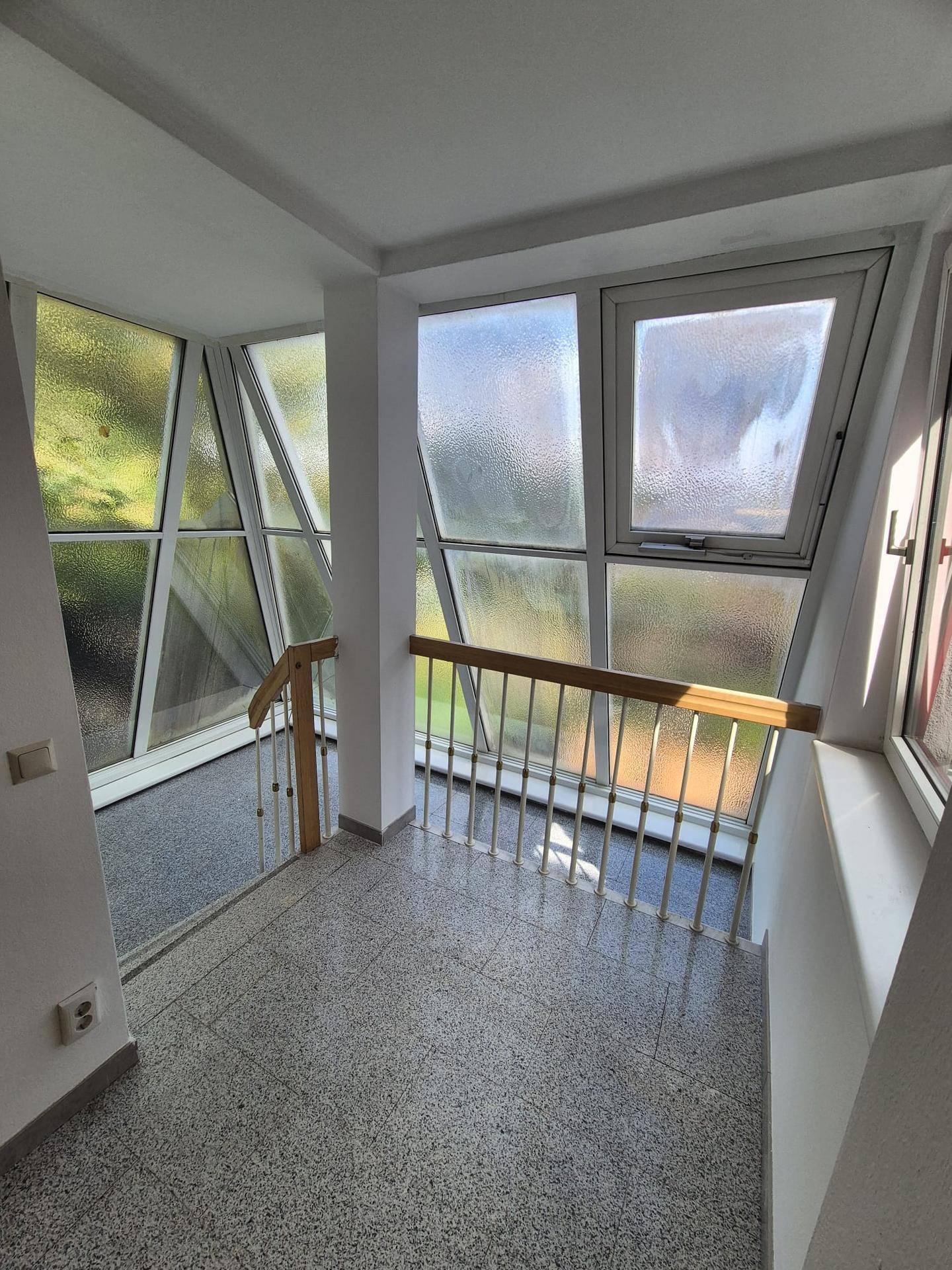 Treppenhaus mit großen, schrägen Fenstern, die viel Tageslicht hereinlassen und einen Blick nach draußen bieten.