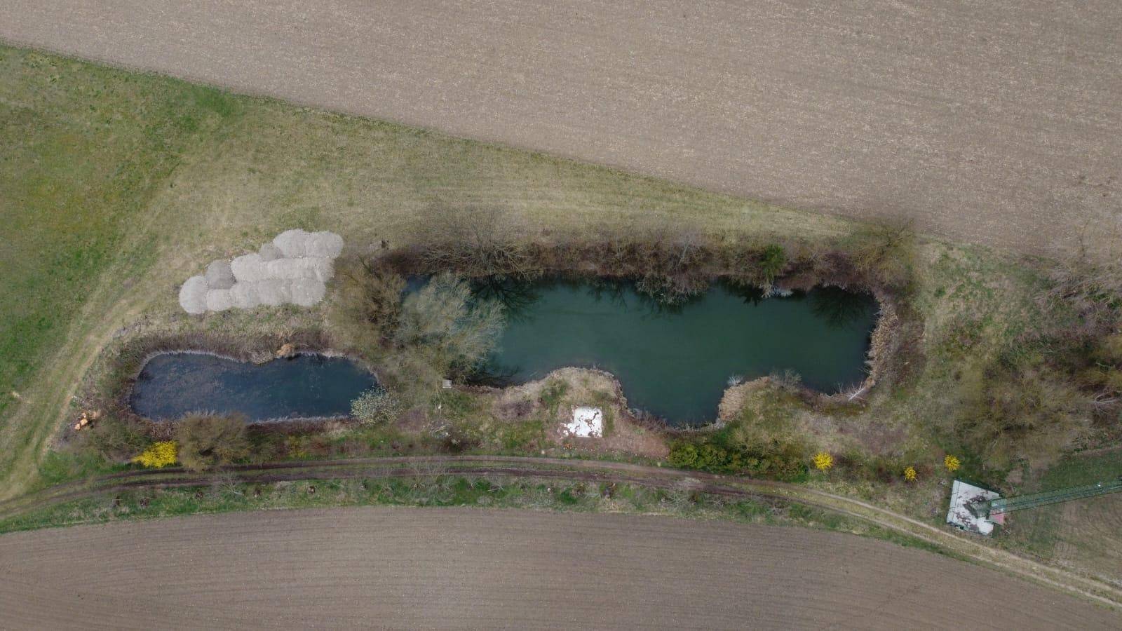 Senkrechte Luftaufnahme der Teiche, umgeben von Feldern und einem Kieshaufen am Rand.