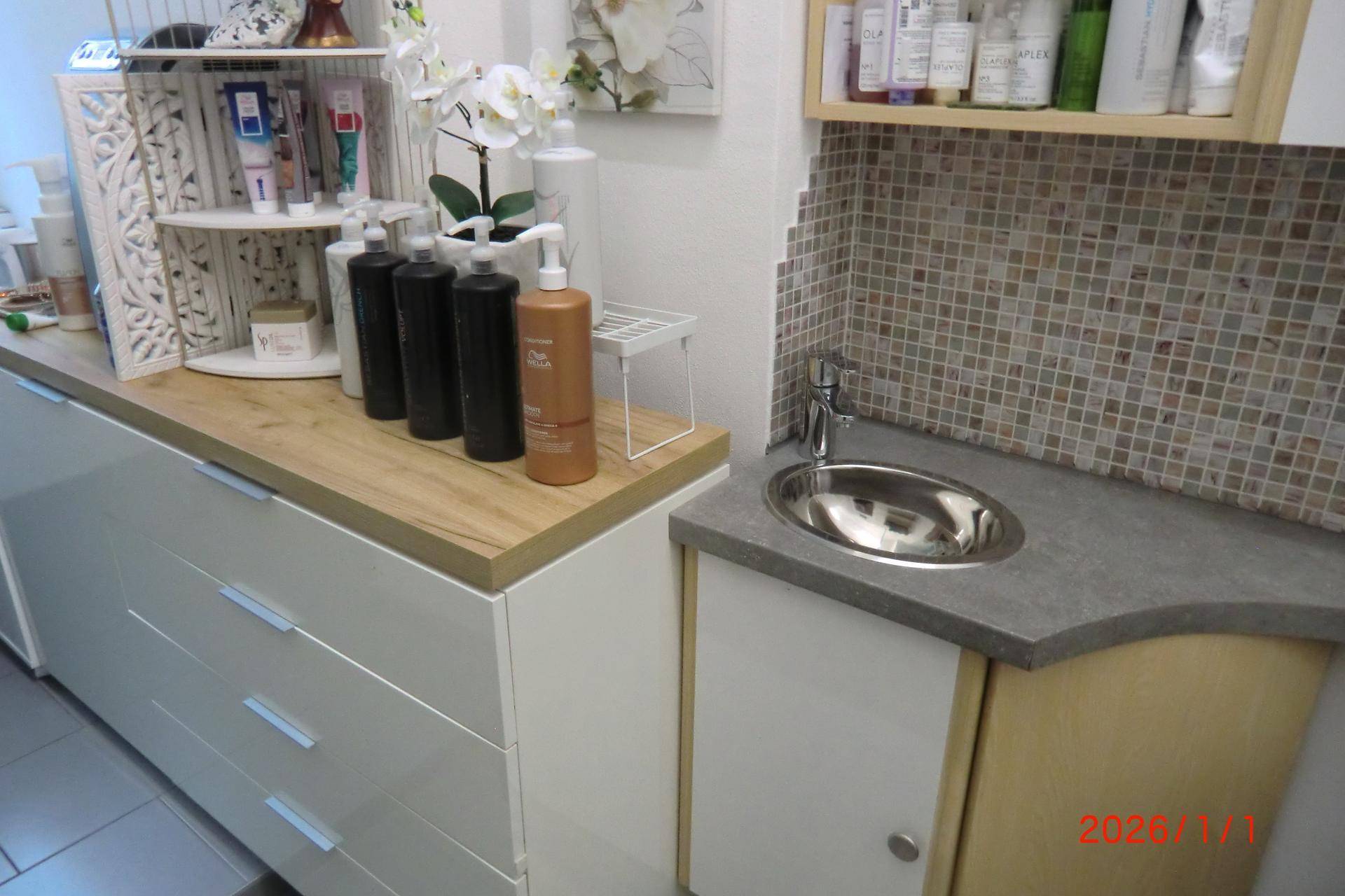Arbeitsbereich mit Waschbecken, Mosaikfliesen und Holztheke für Friseurprodukte.