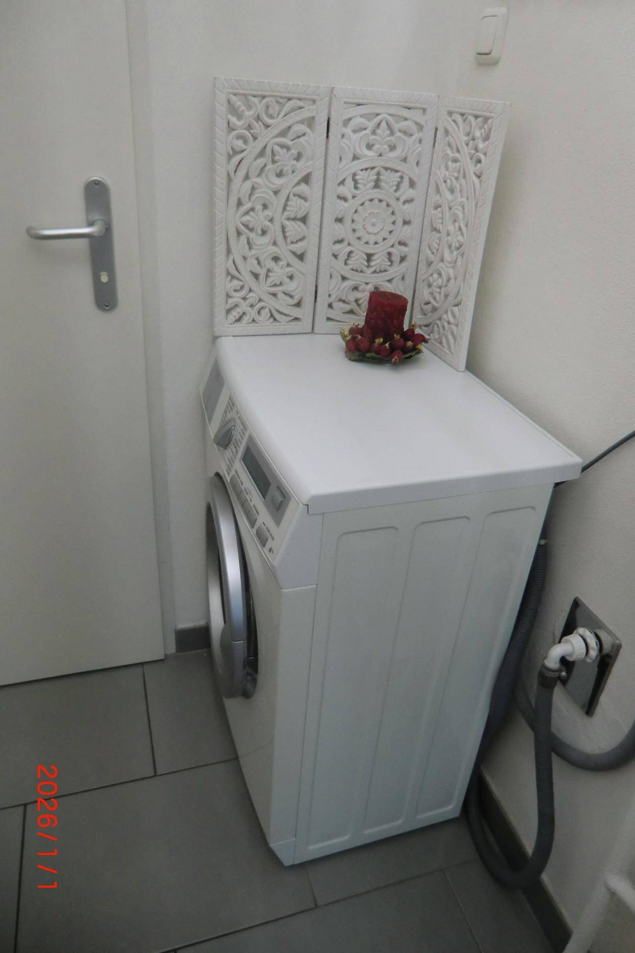 Waschmaschine in einem separaten Bereich mit Fliesenboden und dekorativem Paravent.