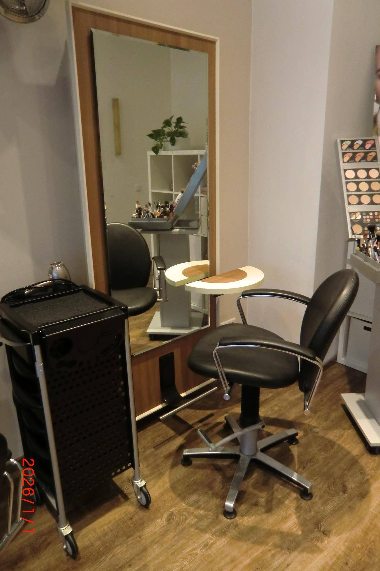 Nahaufnahme eines Friseurstuhls und Spiegels mit mobilem Servierwagen auf Holzfußboden.