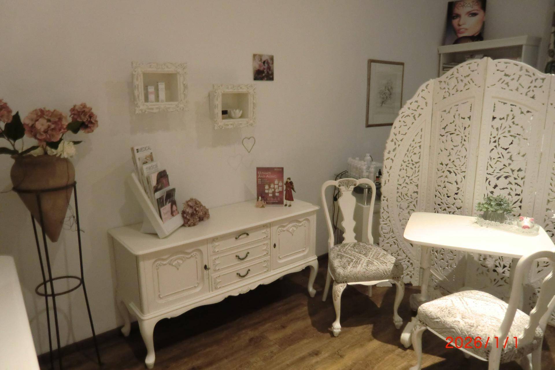 Detailansicht des Behandlungsbereichs mit weißem Sideboard, Blumendekoration und Paravent.