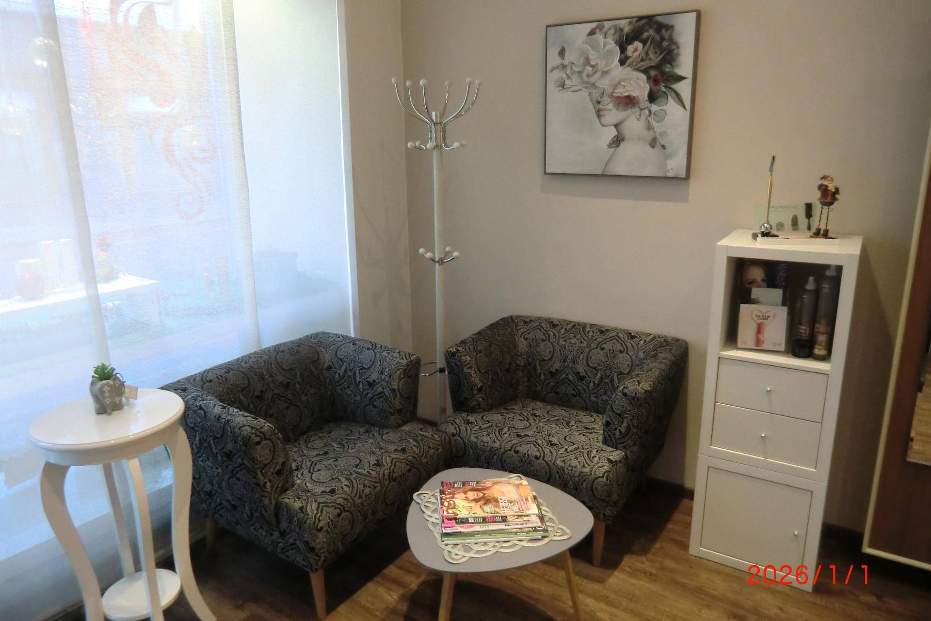 Gemütlicher Wartebereich im Salon mit zwei gepolsterten Sesseln, Beistelltisch und Fenster.