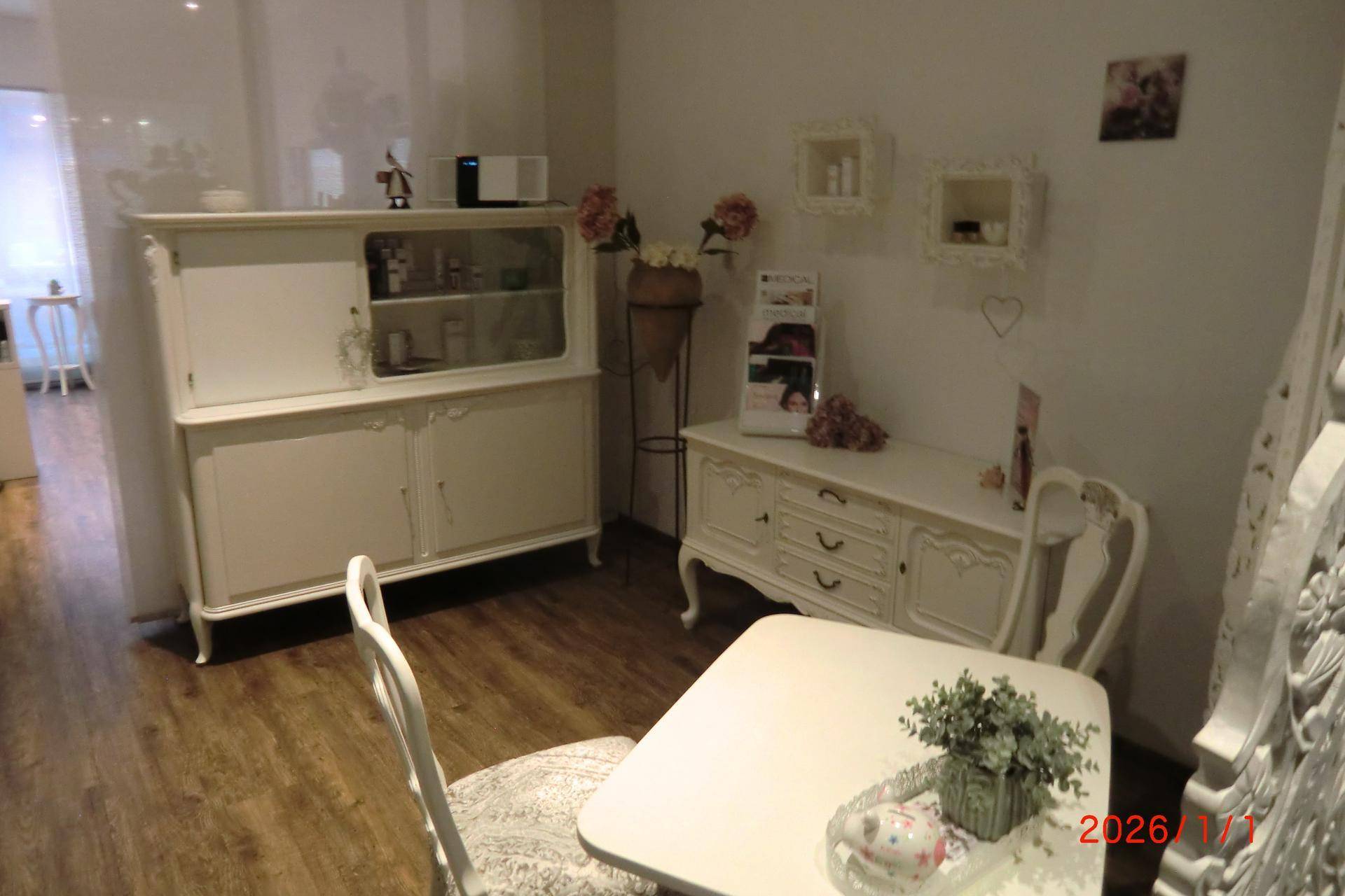 Behandlungsbereich mit weißem Vitrinenschrank, Sideboard und Tisch auf Holzfußboden.