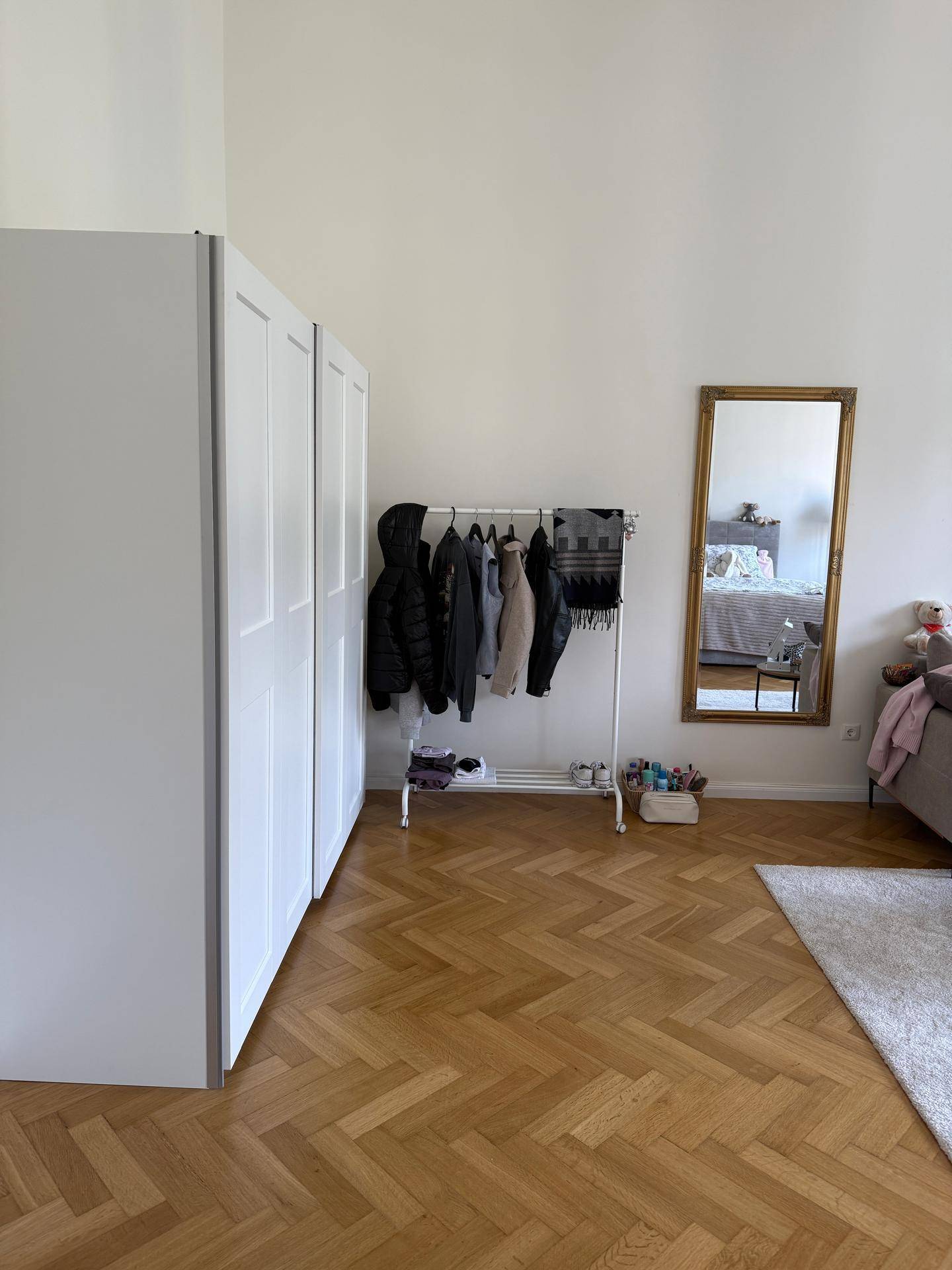 Hoher Raum mit weißem Kleiderschrank, Kleiderstange und großem Spiegel, der den Raum erweitert.