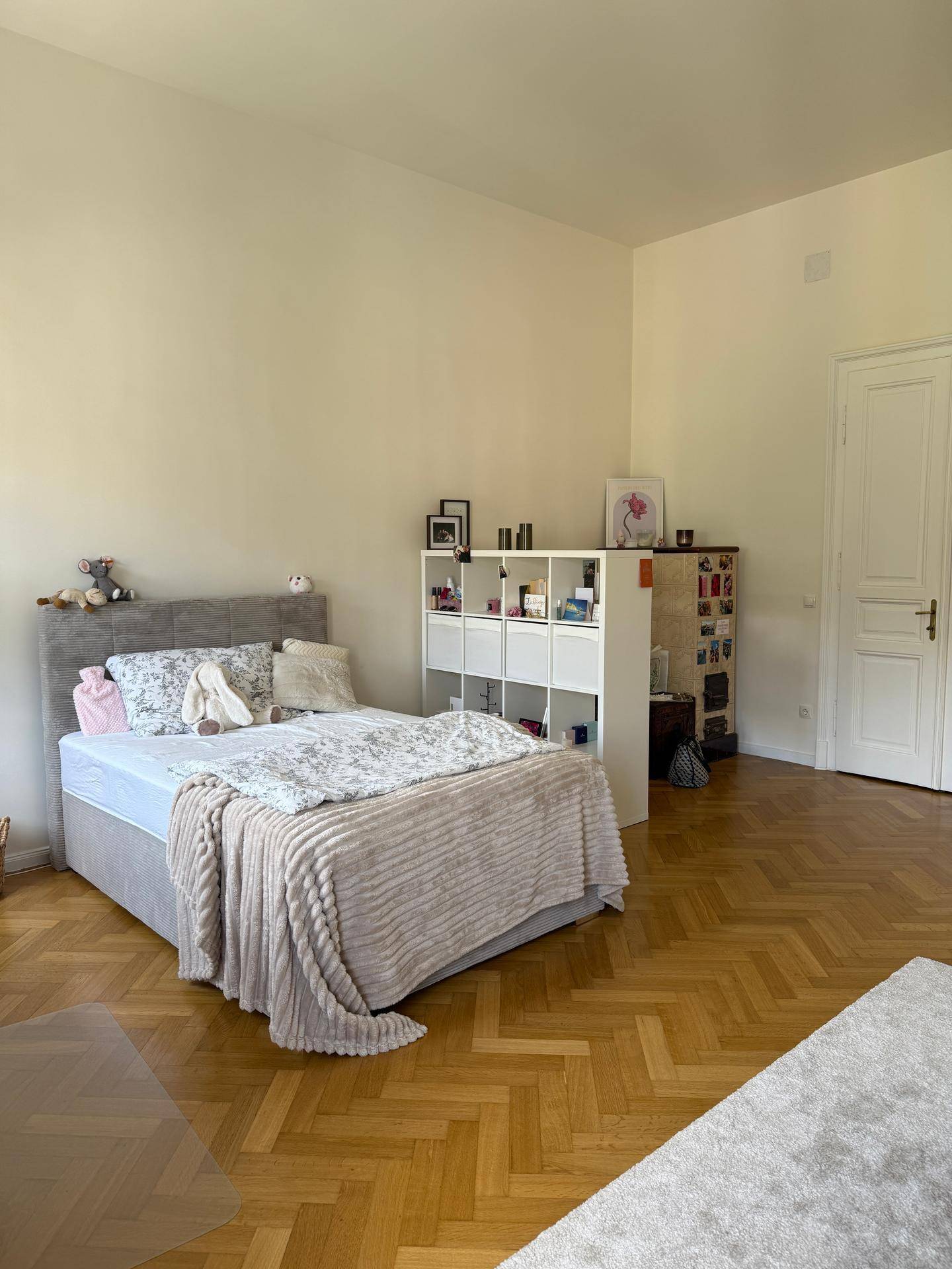 Helles Schlafzimmer mit bequemem Bett, Holzparkett und einem weißen Regal für persönlichen Stauraum.