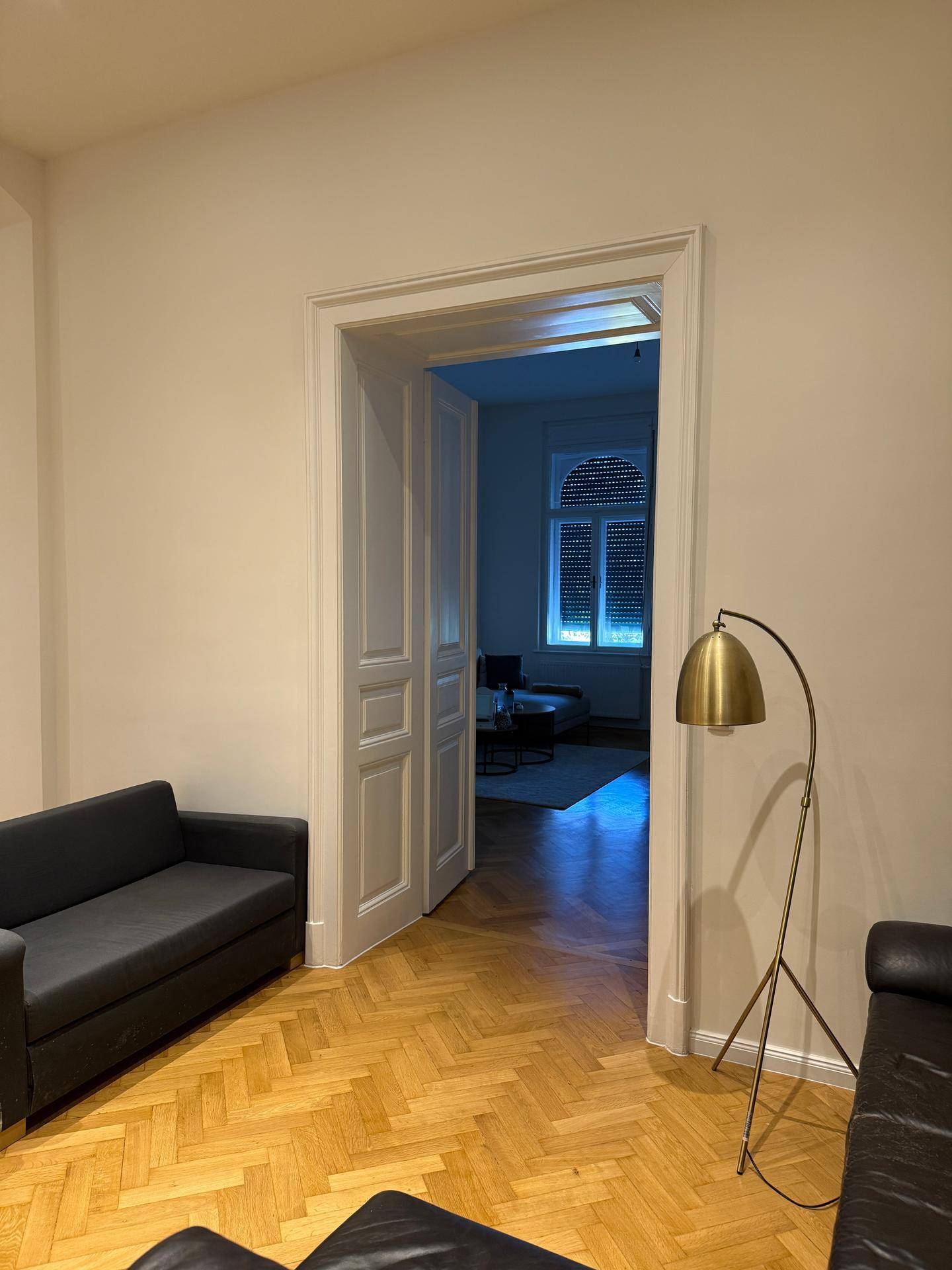 Wohnzimmer mit Fischgrätparkett und offener Tür zu einem weiteren Raum, der viel Licht bietet.