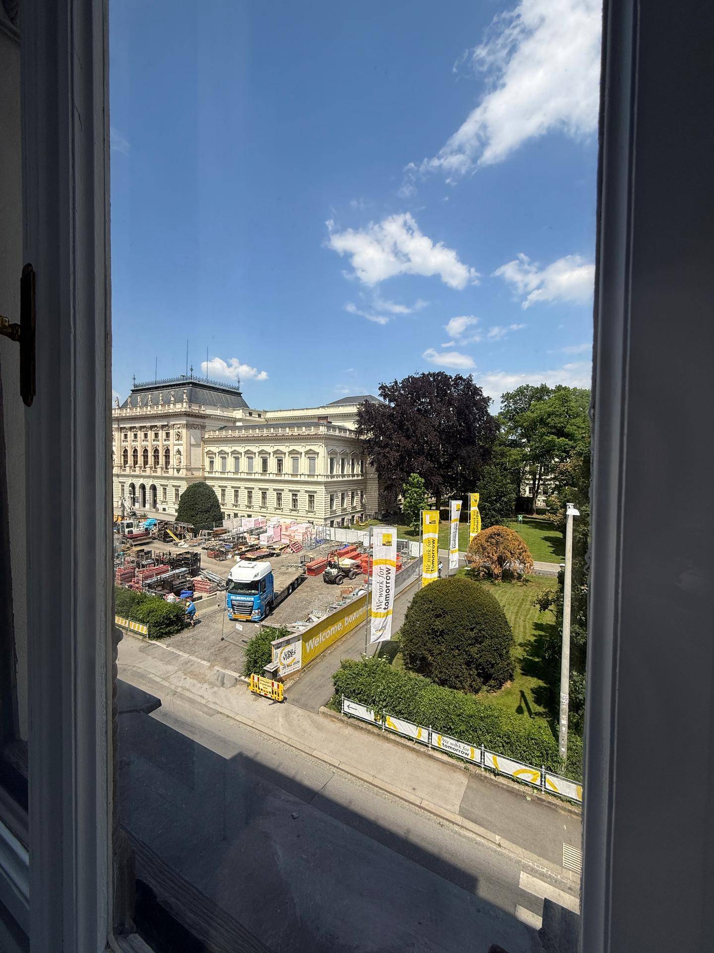 Blick aus dem Fenster auf eine Baustelle und ein historisches Gebäude unter blauem Himmel.