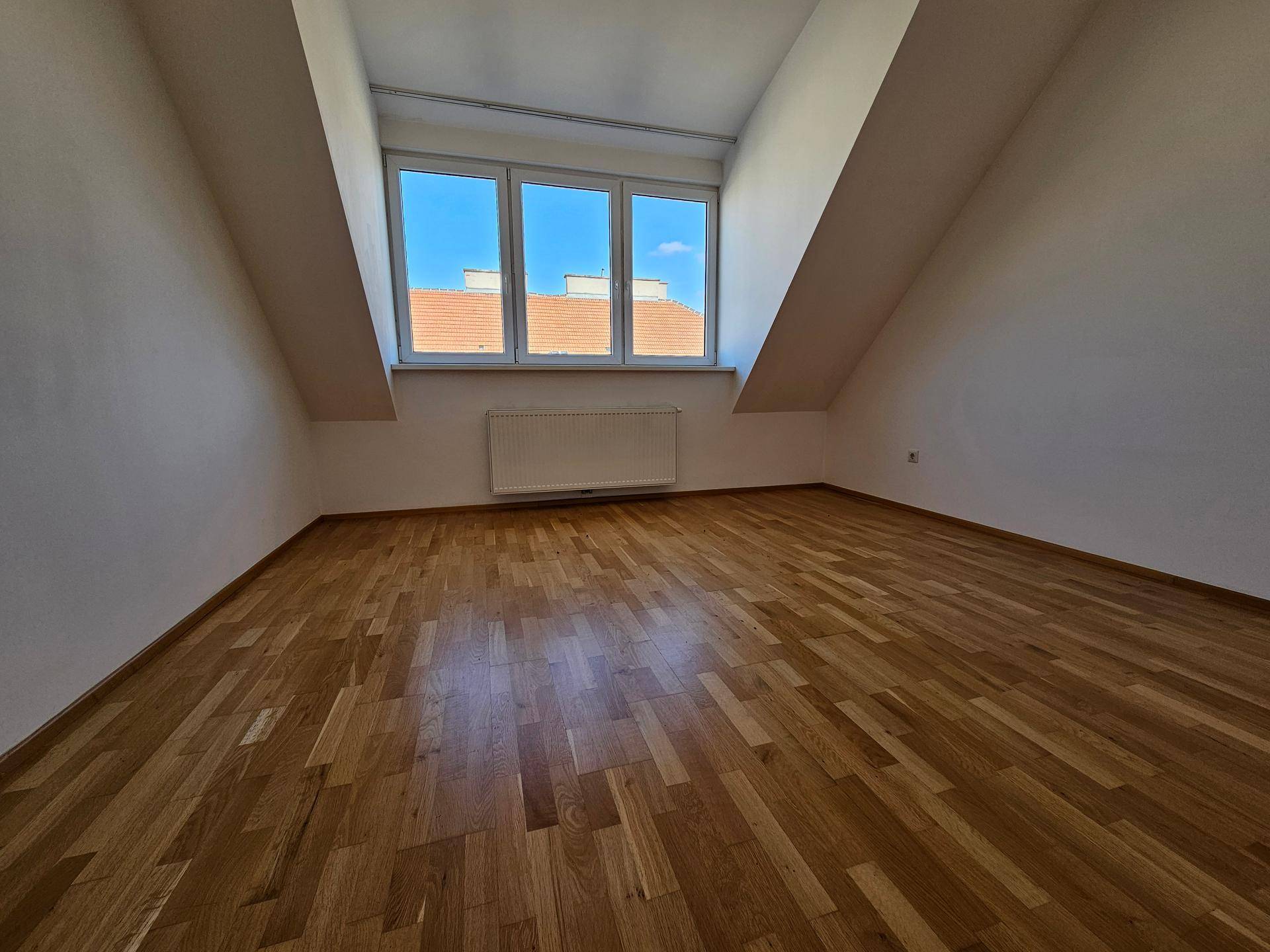 Geräumiges Schlafzimmer mit Holzboden, Dachschräge und drei Fenstern für viel Licht.