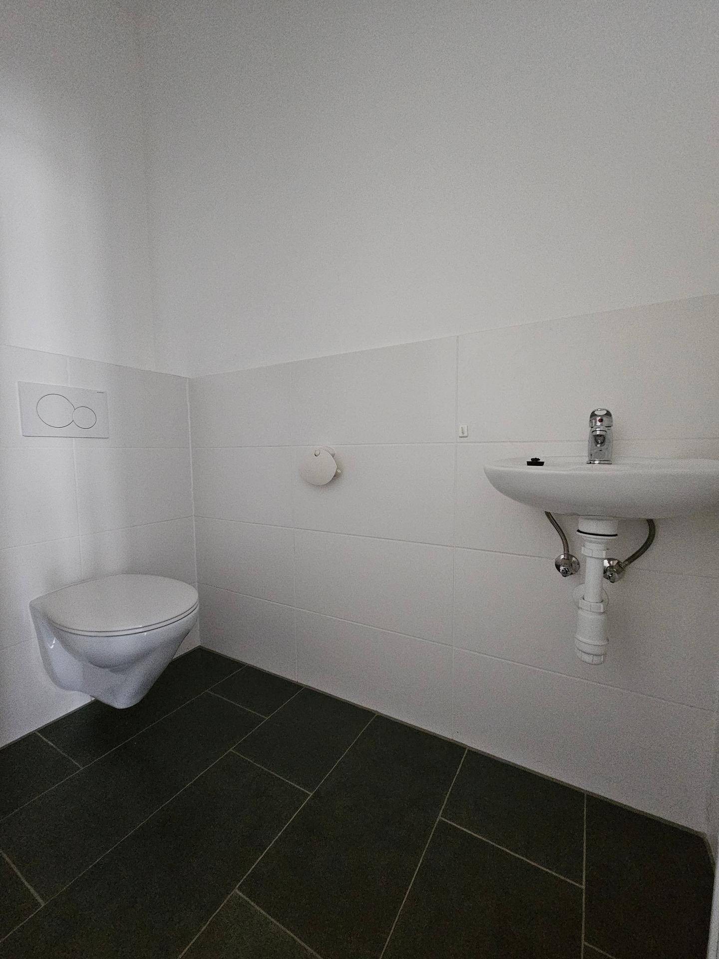 Separates WC mit wandhängender Toilette und kleinem Waschbecken, modern gefliest.