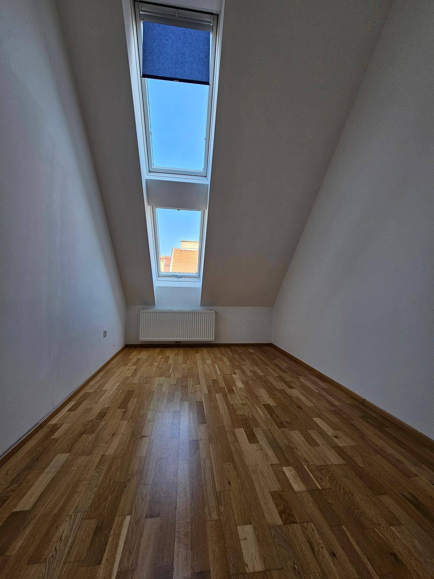 Schlafzimmer mit Holzboden, Dachschräge und zwei hellen Dachfenstern für viel Tageslicht.
