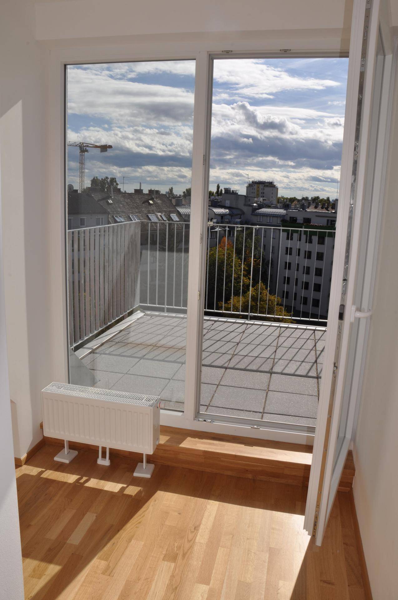 Innenraum mit Holzboden und Zugang zu einem Balkon, der einen weiten Blick über die Stadt bietet.