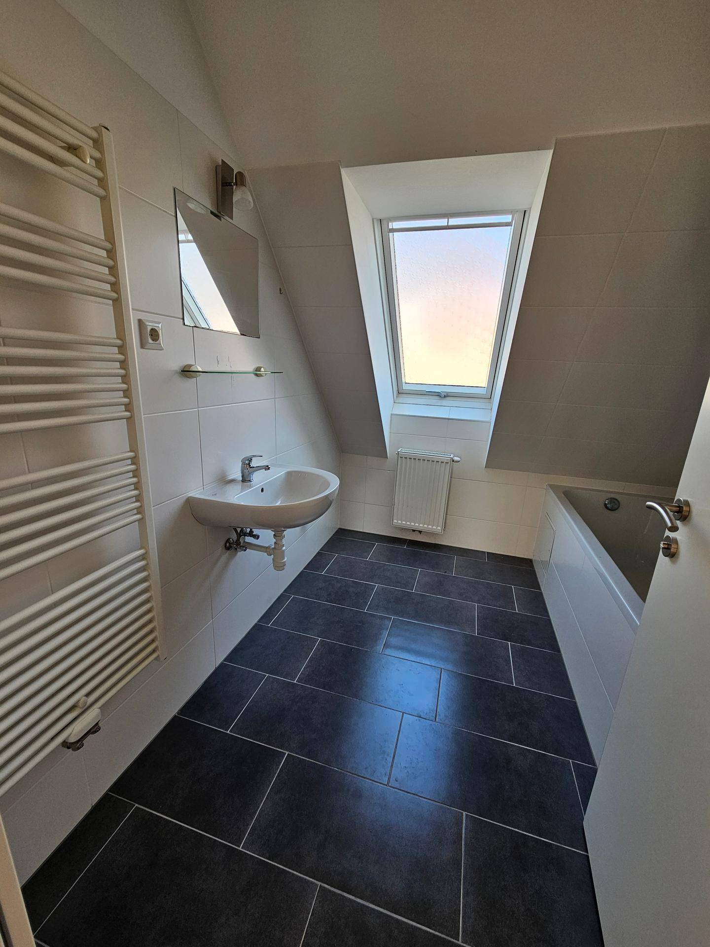 Modernes Badezimmer mit dunklen Fliesen, Badewanne, Waschbecken und Dachfenster.