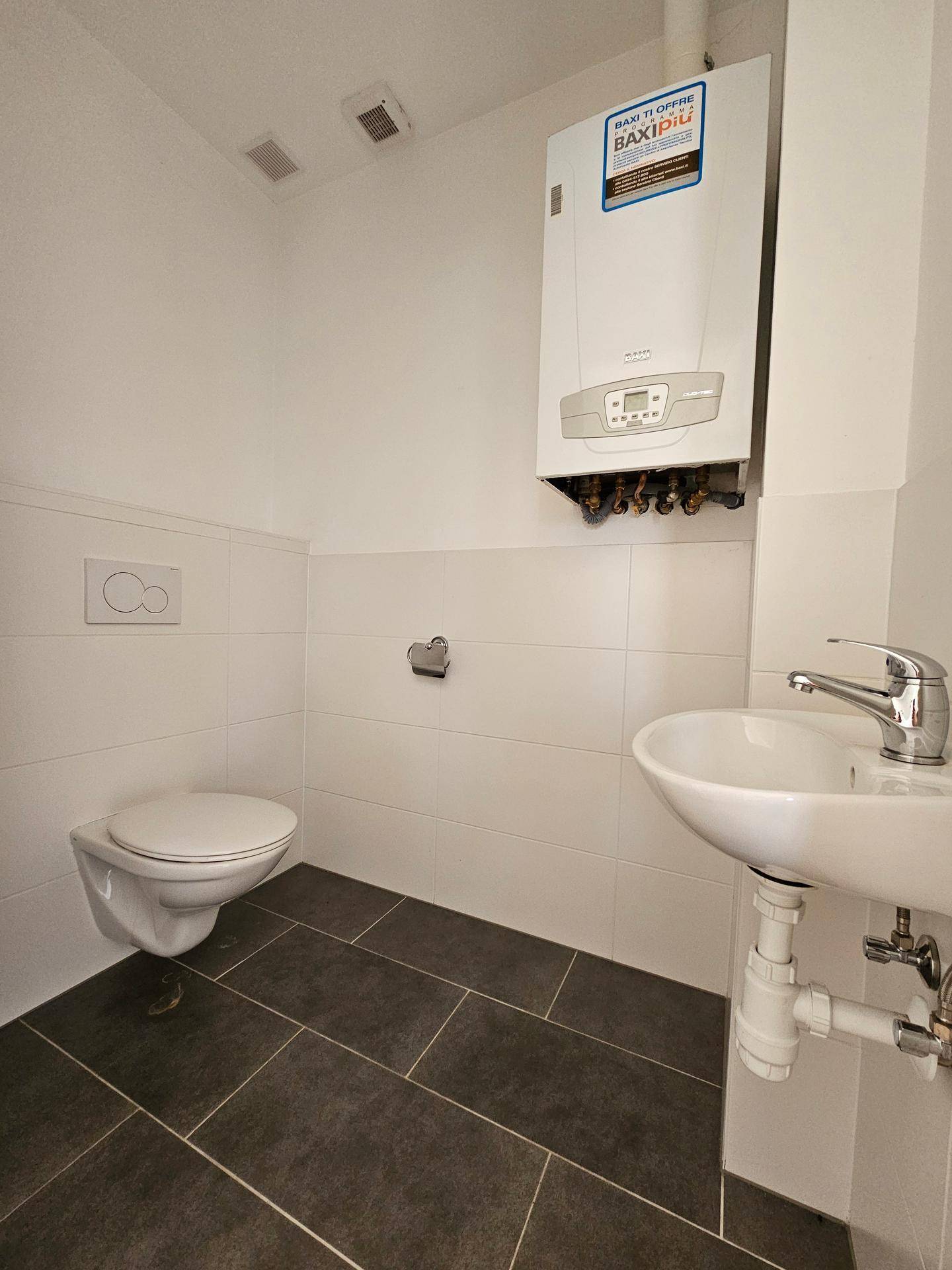 Gäste-WC mit wandhängender Toilette, Waschbecken und einem Warmwasserbereiter an der Wand.