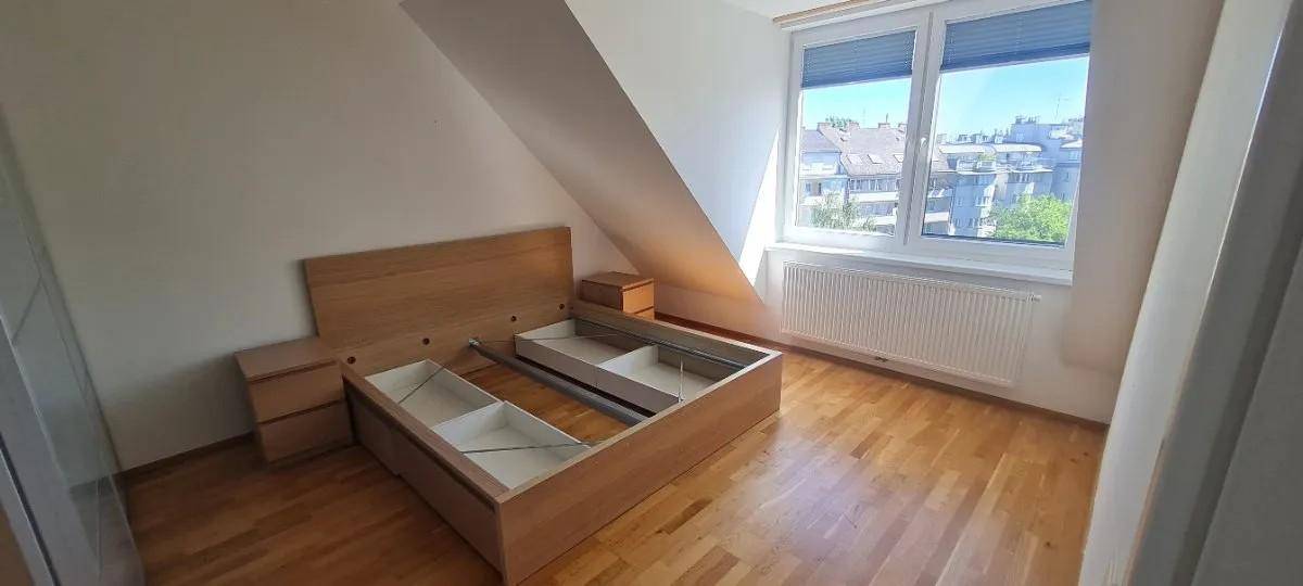 Schlafzimmer mit Holzboden, Dachschräge und einem Bettrahmen mit integriertem Stauraum.