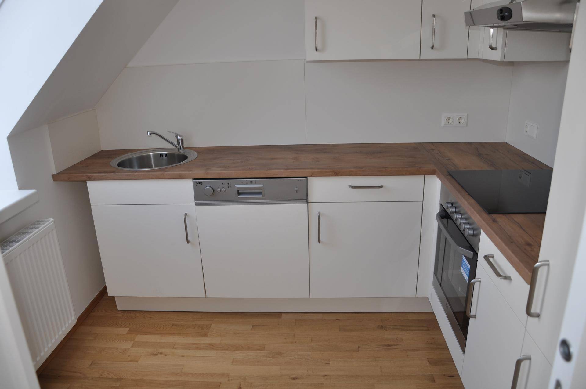 Helle Einbauküche mit weißen Schränken, Holz-Arbeitsplatte und integrierten Geräten unter einer Dachschräge.