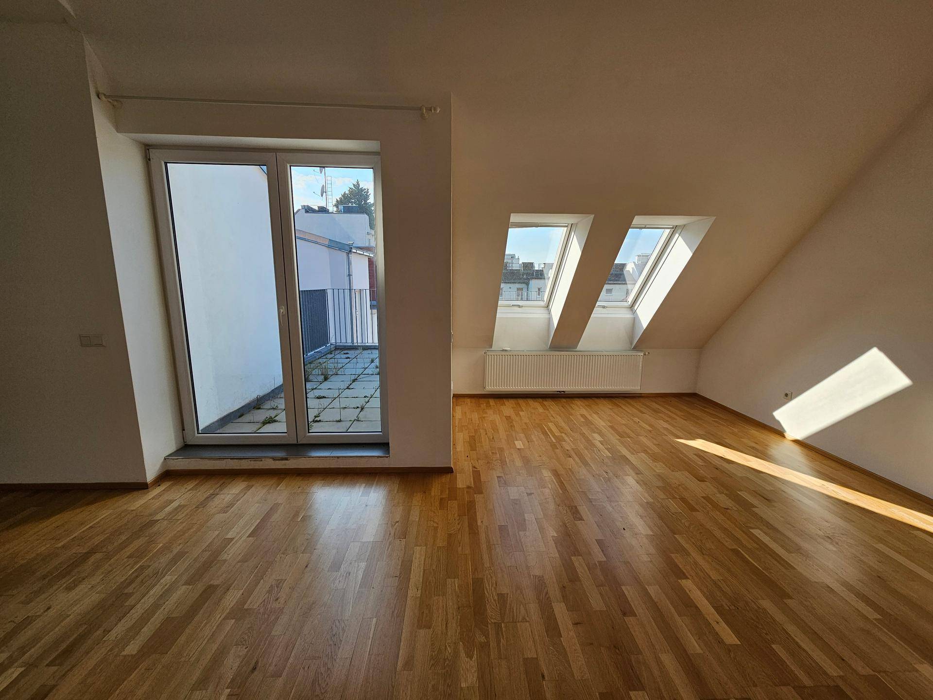 Lichtdurchfluteter Wohnbereich mit Holzboden, Dachschrägen und mehreren Dachfenstern.