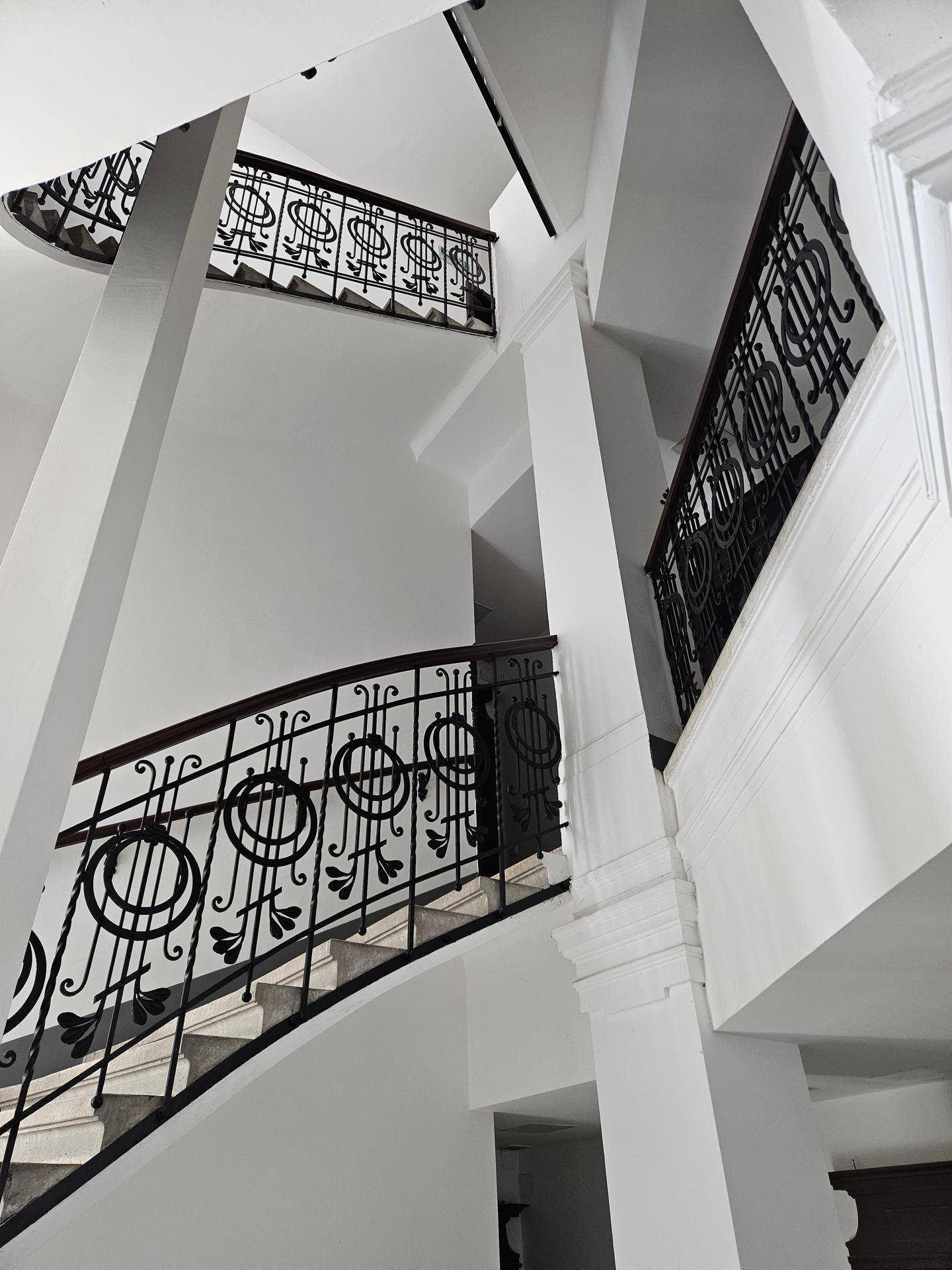 Elegantes Treppenhaus mit kunstvollen schmiedeeisernen Geländern und hohen, hellen Wänden.