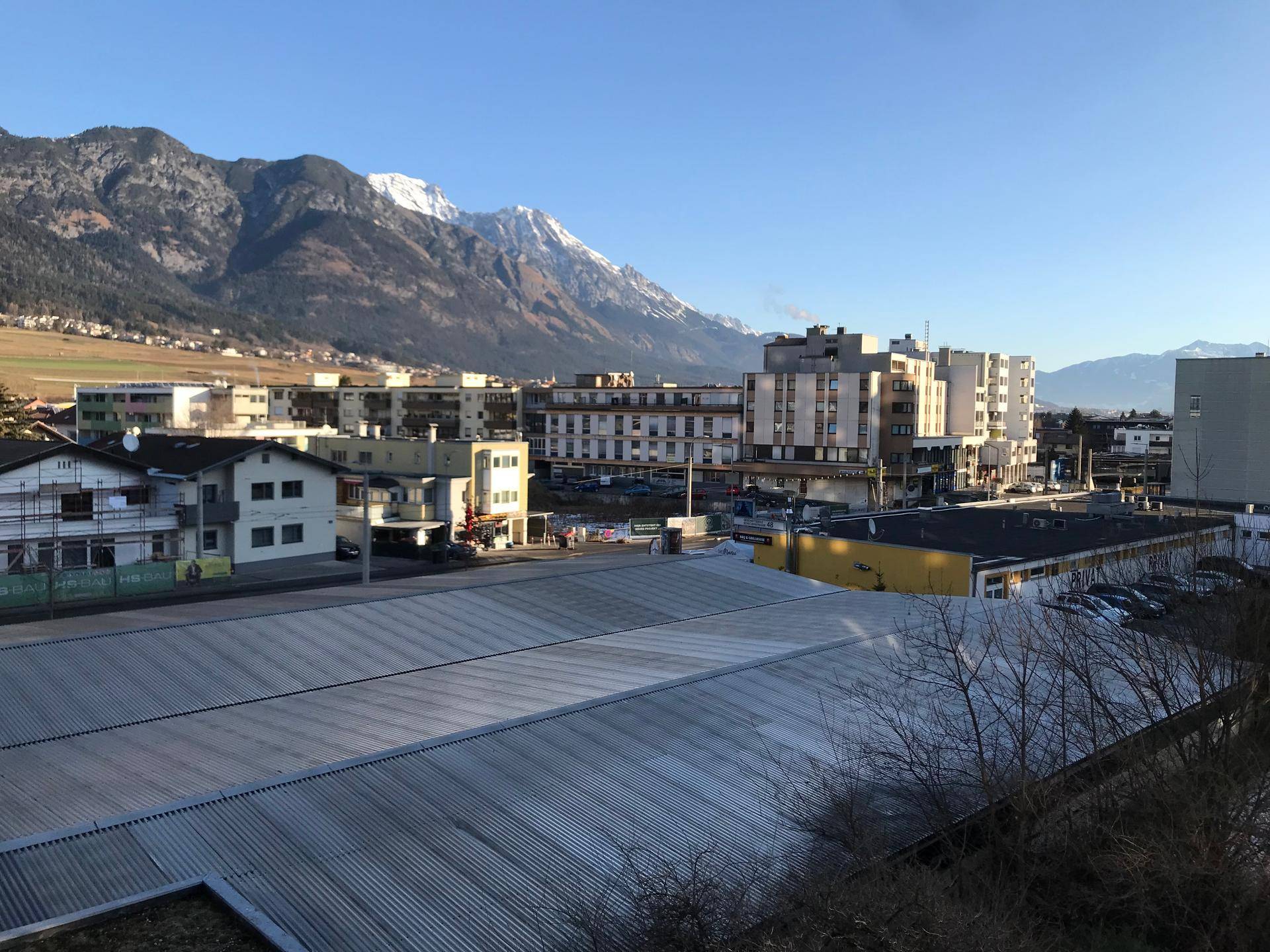 Weitläufiger Blick über städtische Dächer und Gebäude mit majestätischen Bergen im Hintergrund.