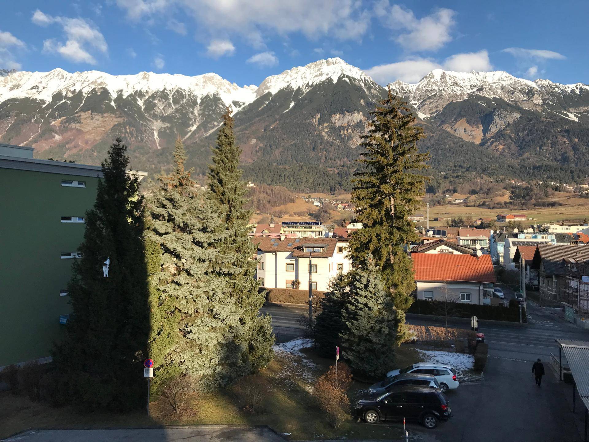 Panoramablick auf schneebedeckte Berge, grüne Bäume und die umliegende Stadtlandschaft.