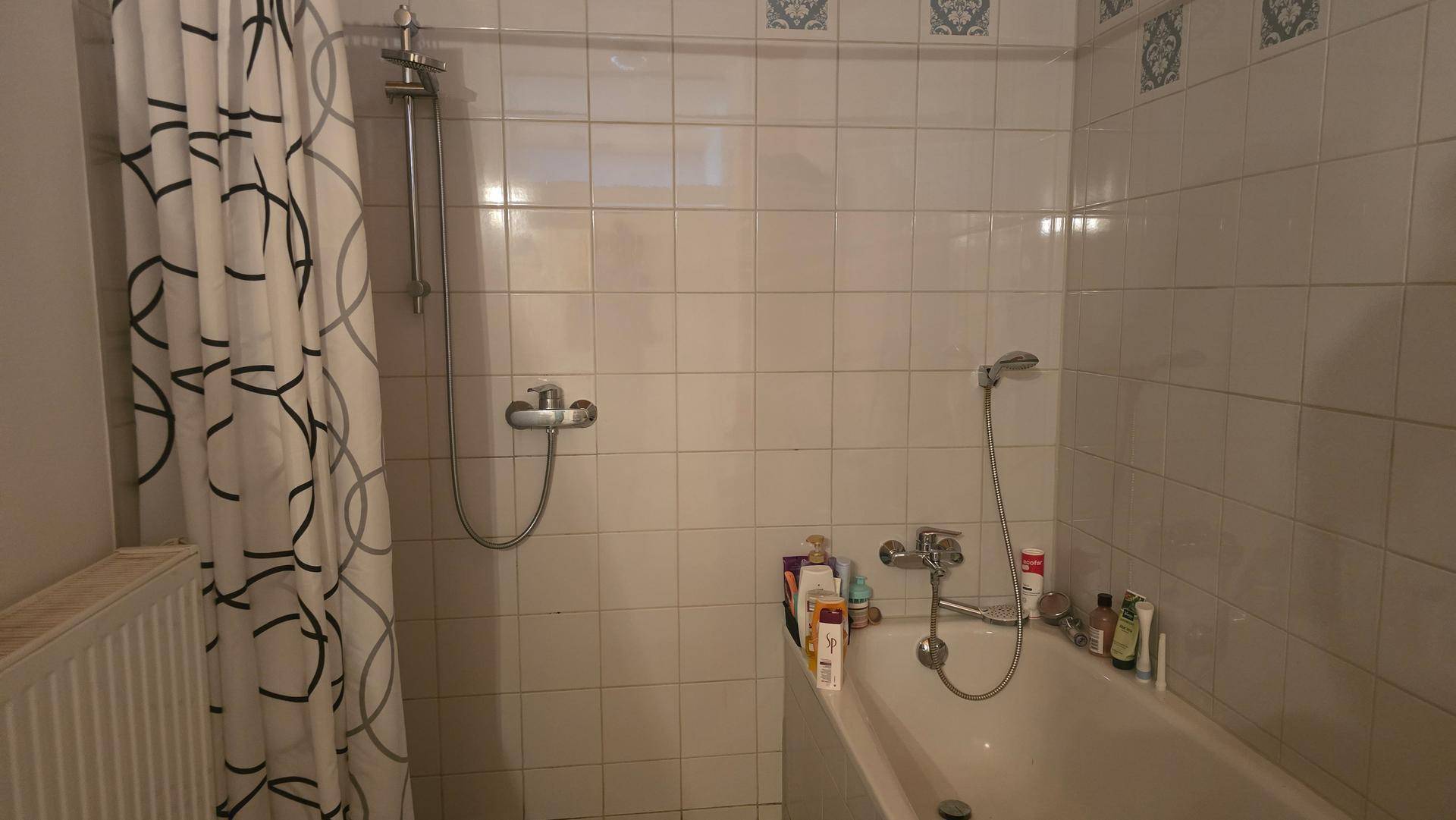 Badezimmer mit Badewanne und Duschvorrichtung, gefliesten Wänden und Heizkörper.