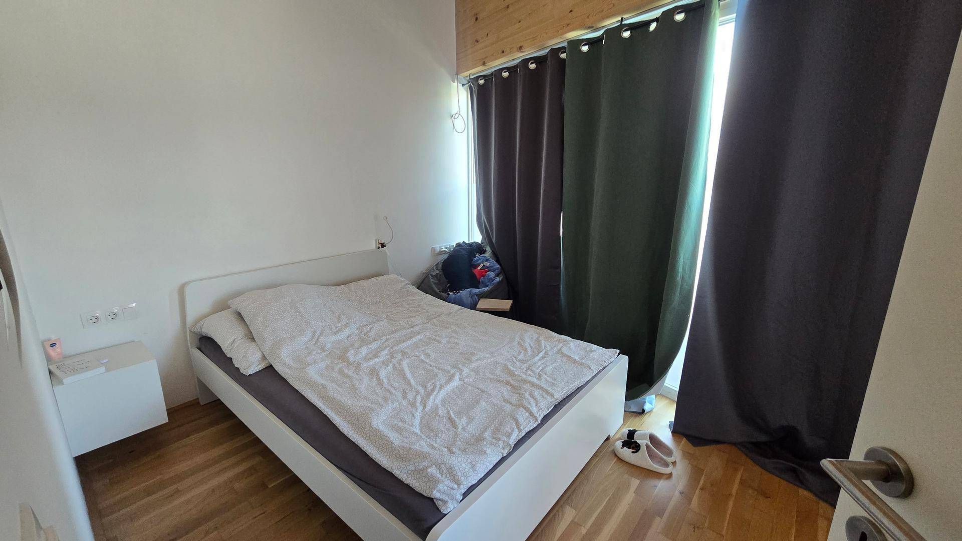 Schlafzimmer mit Einzelbett, Holzboden und Holzdecke, dunkle Vorhänge.