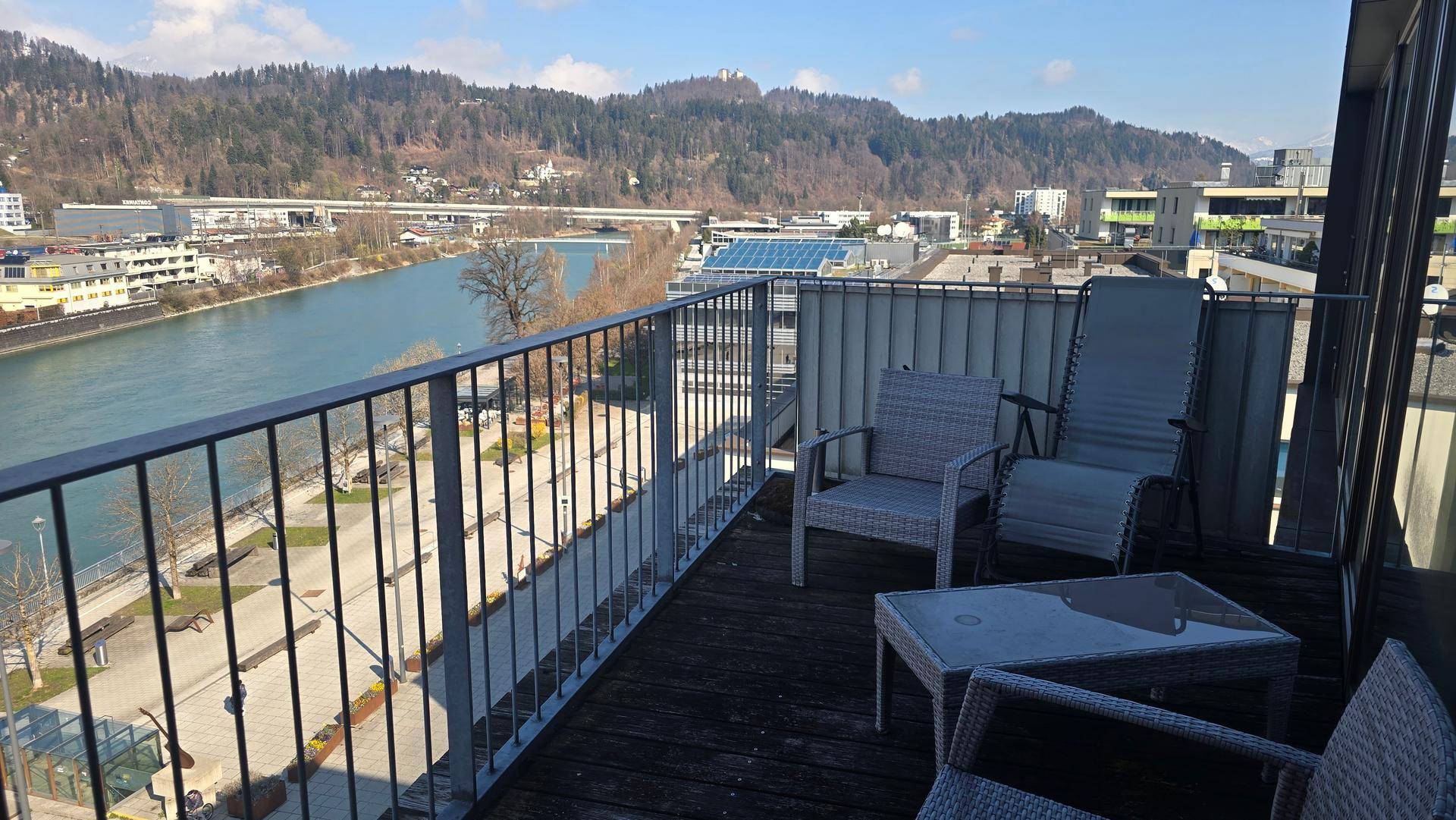 Geräumiger Balkon mit Sitzgelegenheiten, Blick auf den Fluss und die umliegende Berglandschaft.